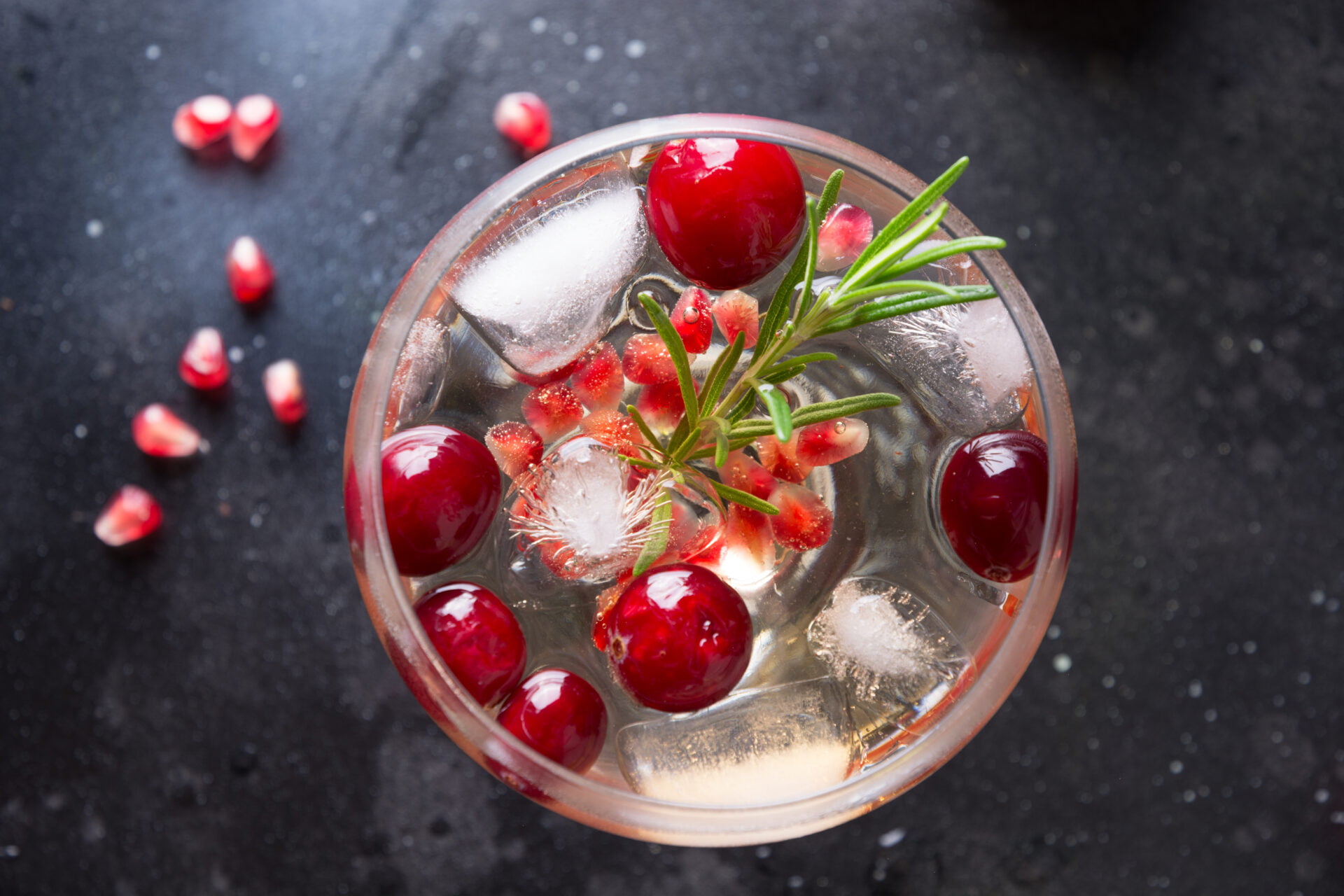 Pomegranate Christmas cocktail with rosemary, club soda on black table