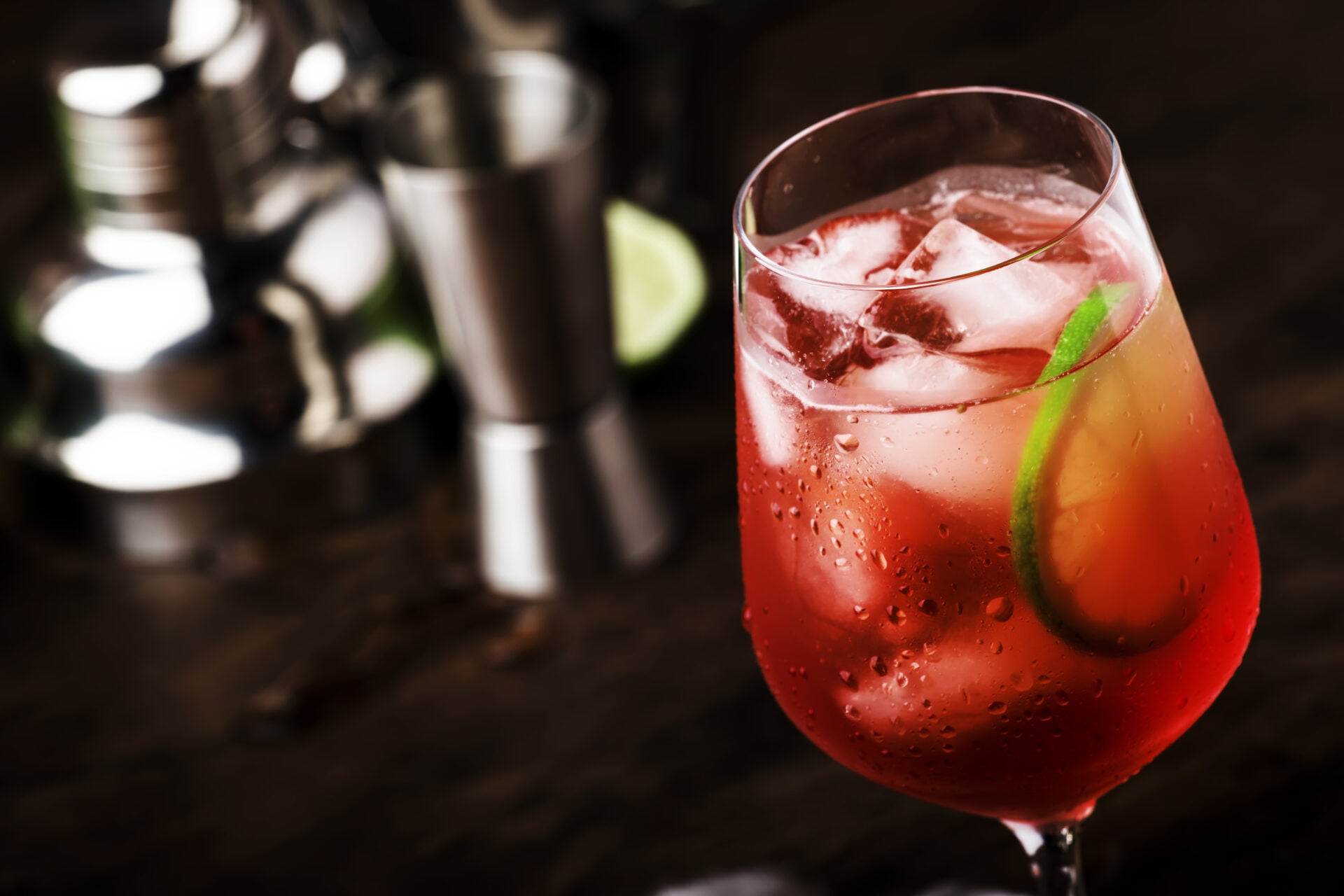 Campari tonic alcoholic cocktail with red bitter, tonic, lime and ice. Old wooden table background & bar tools
