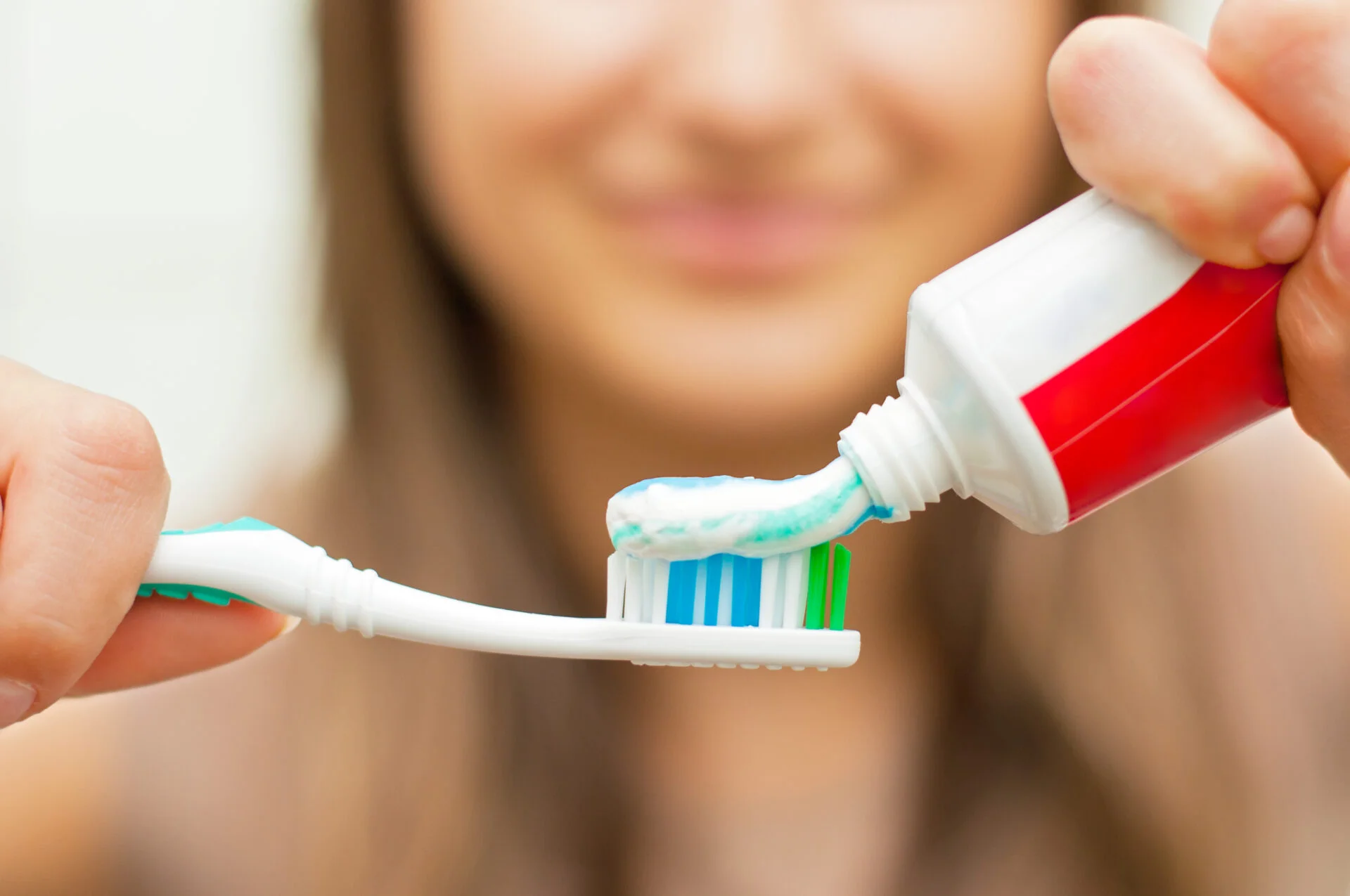 Young woman holding a toothbrush and placing toothpaste on it