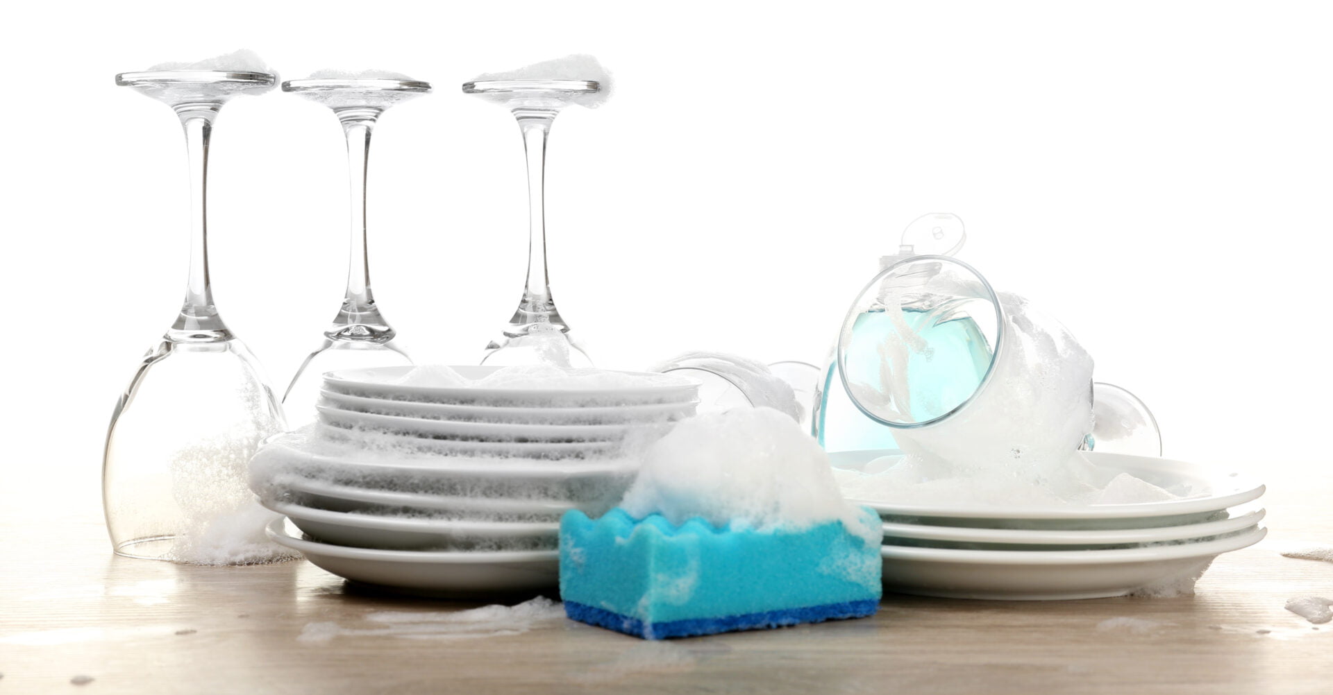 Dishes in foam with gloves and wisp on table isolated on white