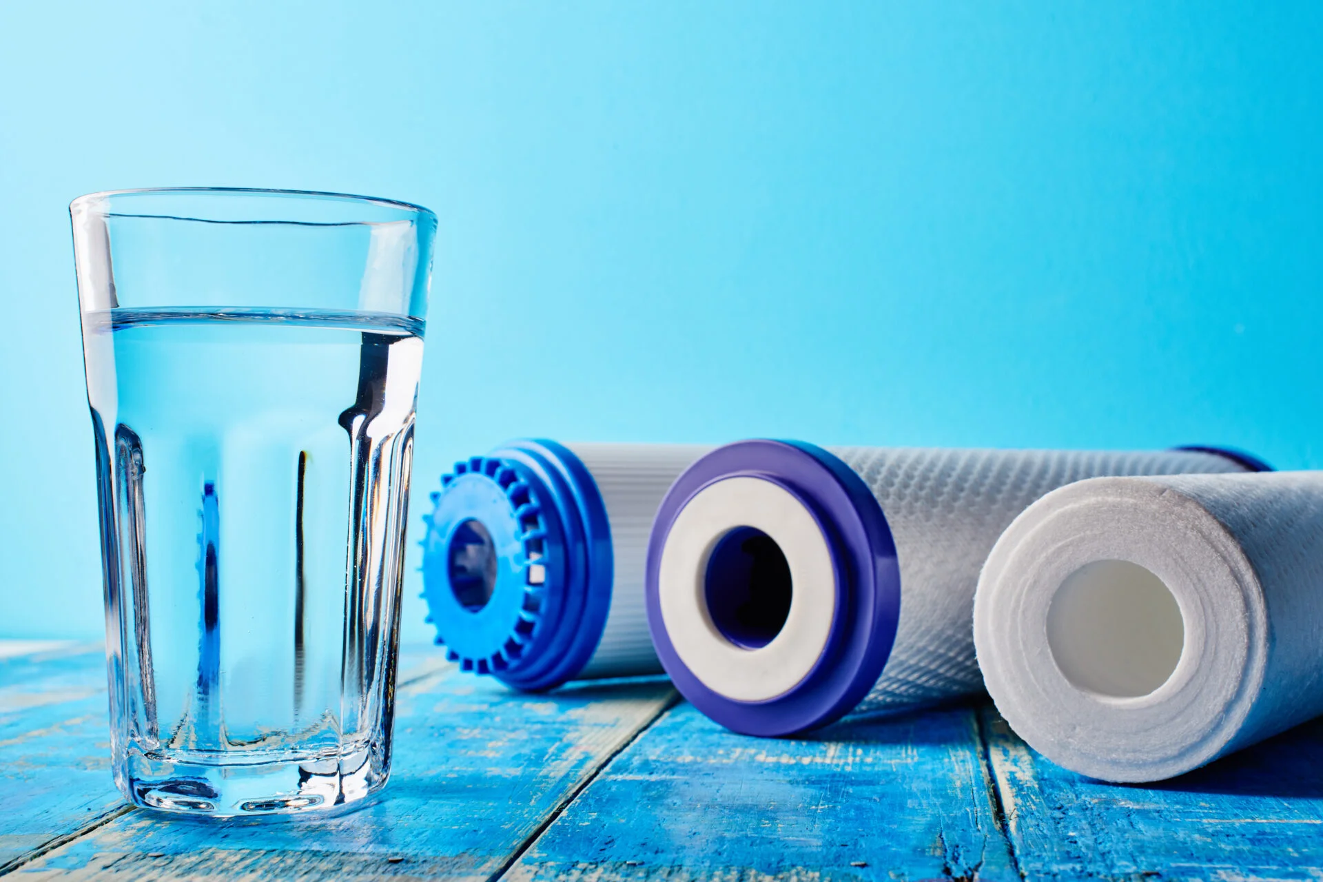 Water filters. Carbon cartridges and a glass on a blue background. Household filtration system