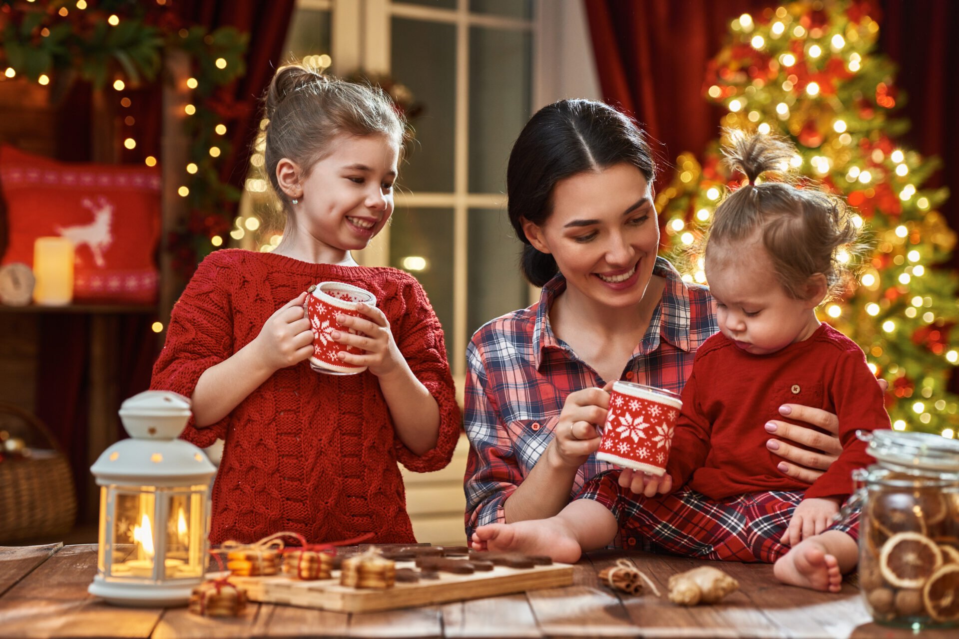 Merry Christmas and Happy Holidays. Time of family tea party. Mother and her children daughters are drinking warm tea with Christmas cookies