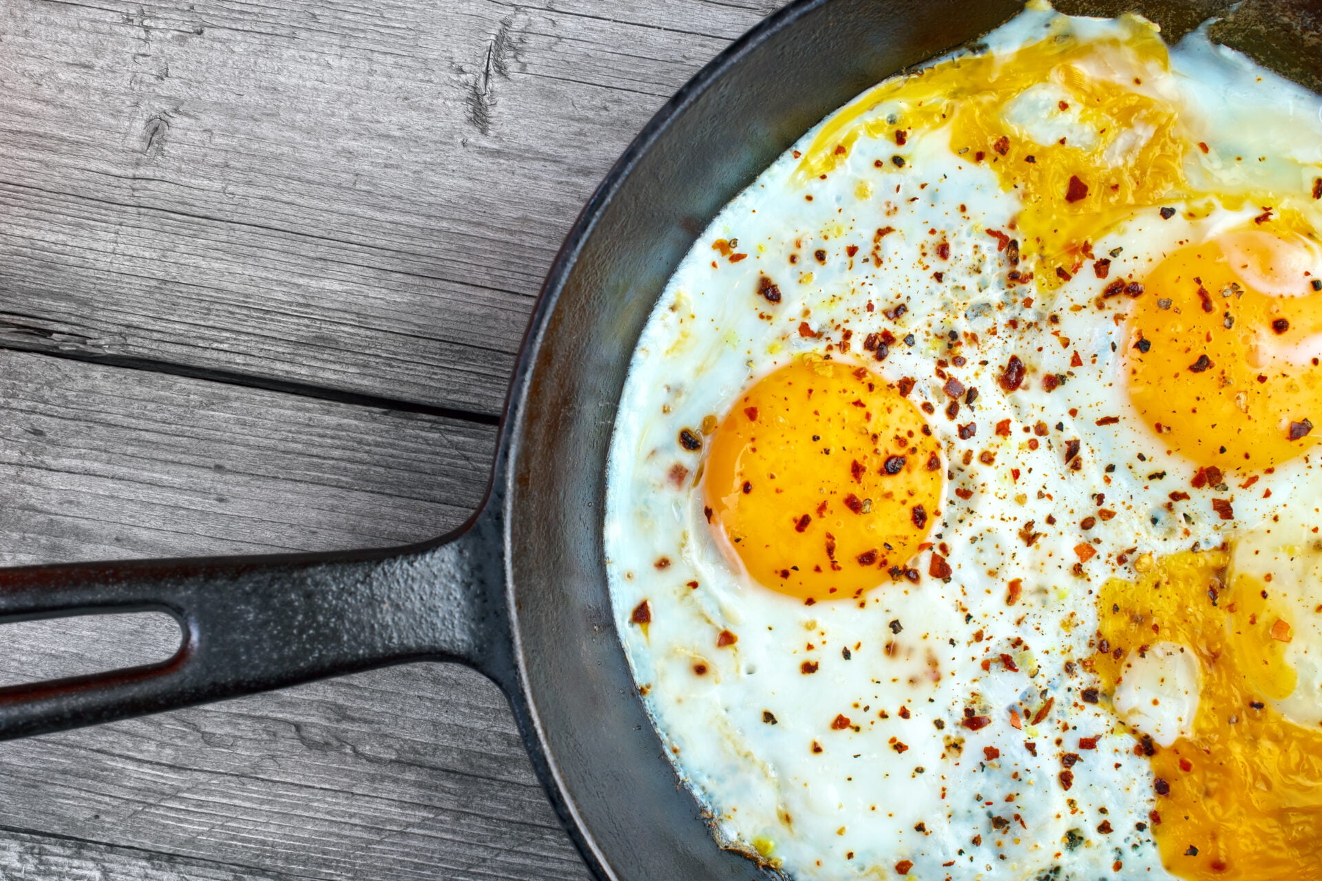 Fried eggs in cast iron frying pan on gray wooden surface 