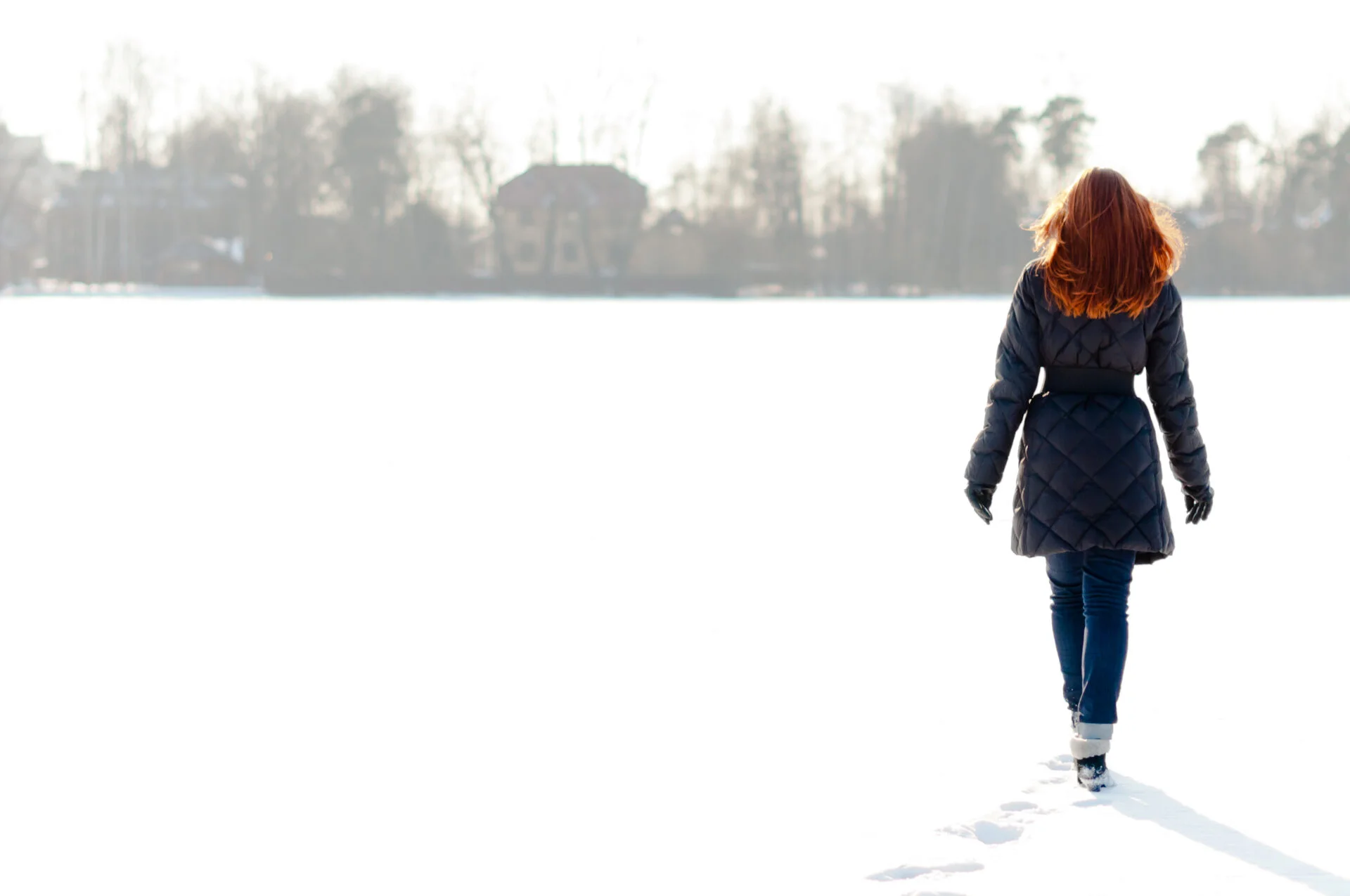 Pretty red haired girl walking on frozen lake and making footpath wearing a PFAS free snow jacket