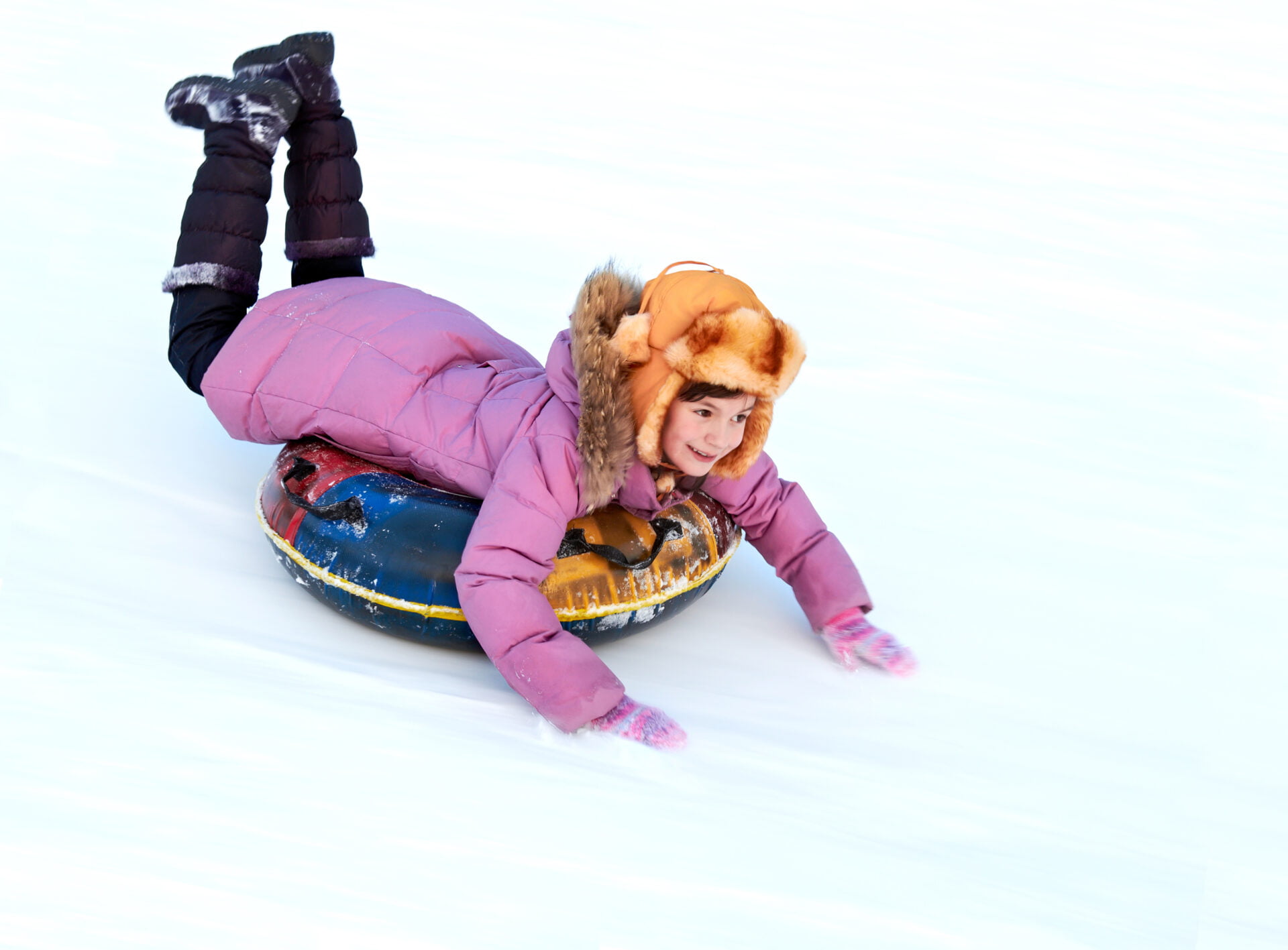 Child riding color covered inner tube down snow cover hill at speed in a PfAS free jacket