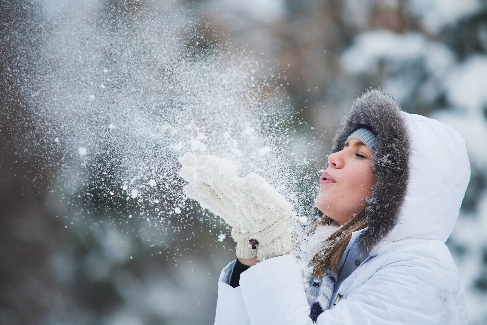 Beautiful woman blowing in the snow wearing a PFAS free jacket