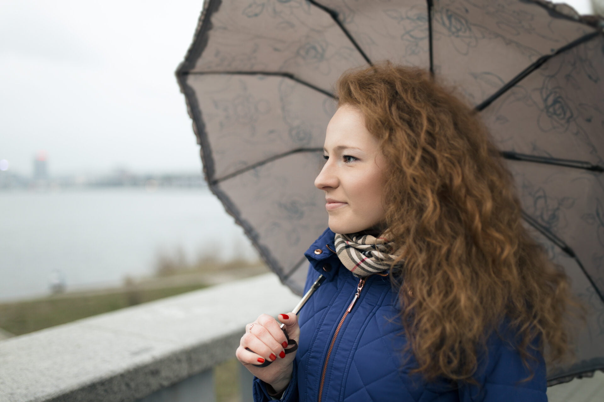 Young woman walking at quay with umbrella on a rainy day