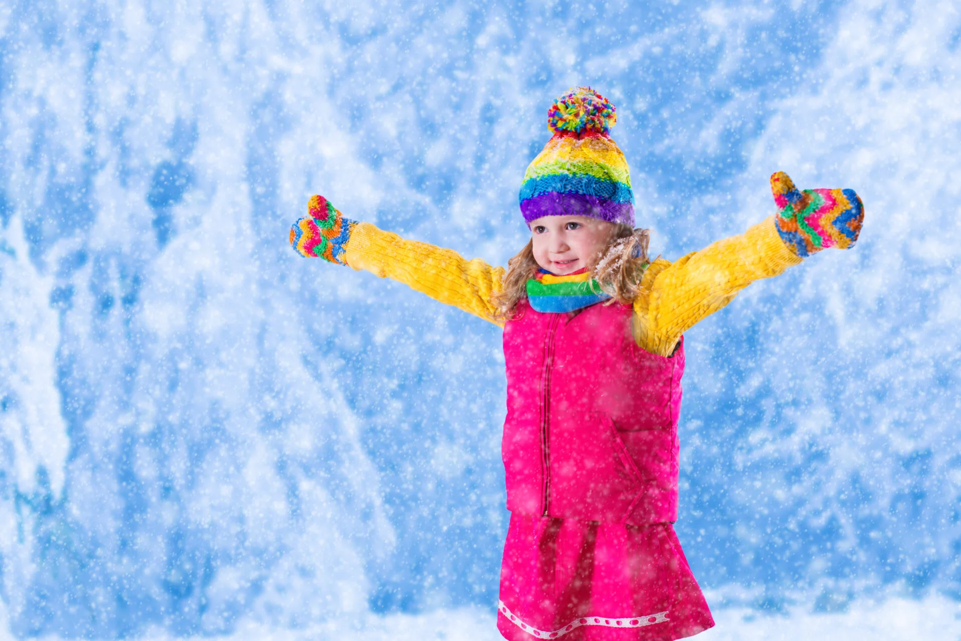 Little girl in pink jacket and colorful knitted hat catching snowflakes in winter park. Kids play outdoor in snowy forest. Children catch snow flakes. Toddler kid playing outside in snow storm
