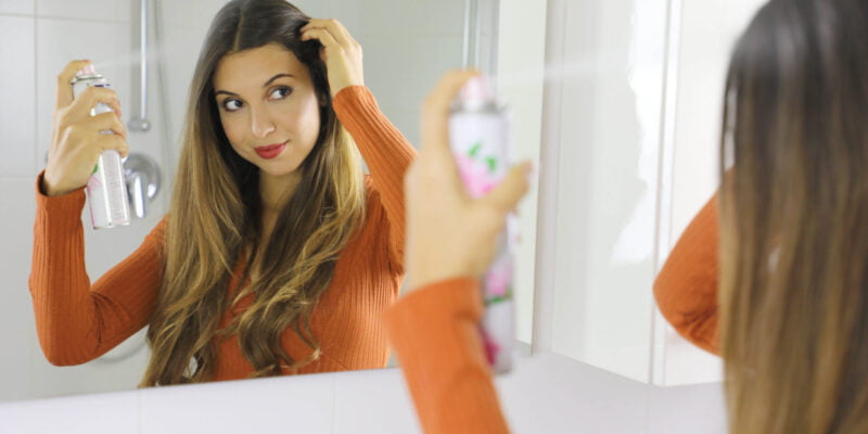 Young woman applying dry shampoo on her hair. Fast and easy way to keep hair clean with dry shampoo