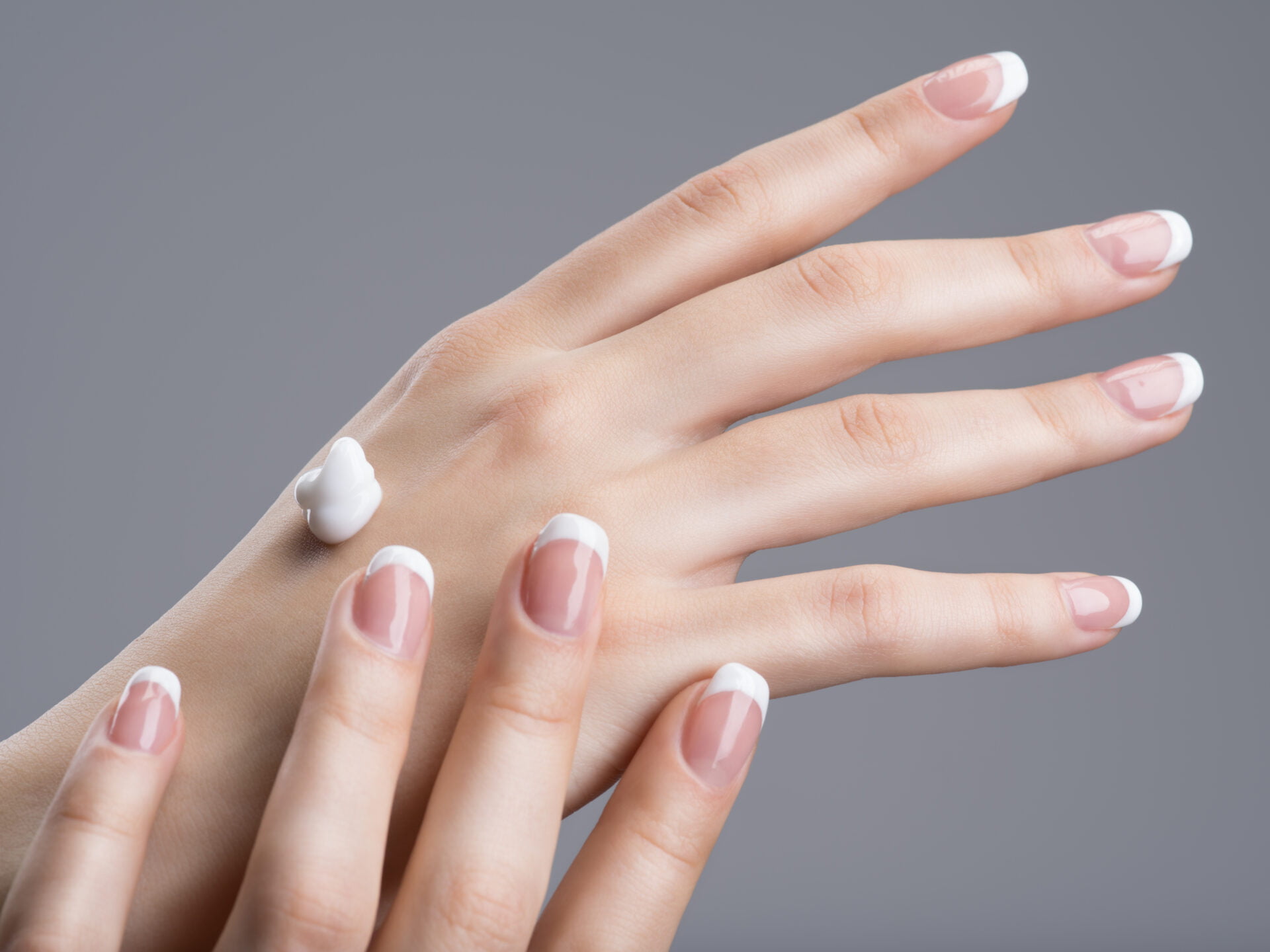 Close-up female hands apllying hand cream. with french manicure on nails