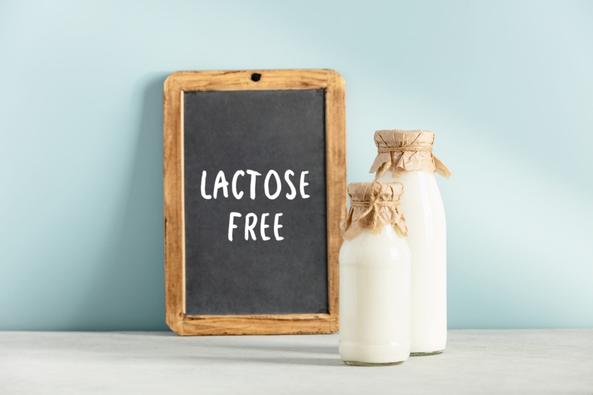 Non dairy plant based milk in bottles and chalkboard with Lactose free lettering on light blue background. Alternative lactose free milk substitute