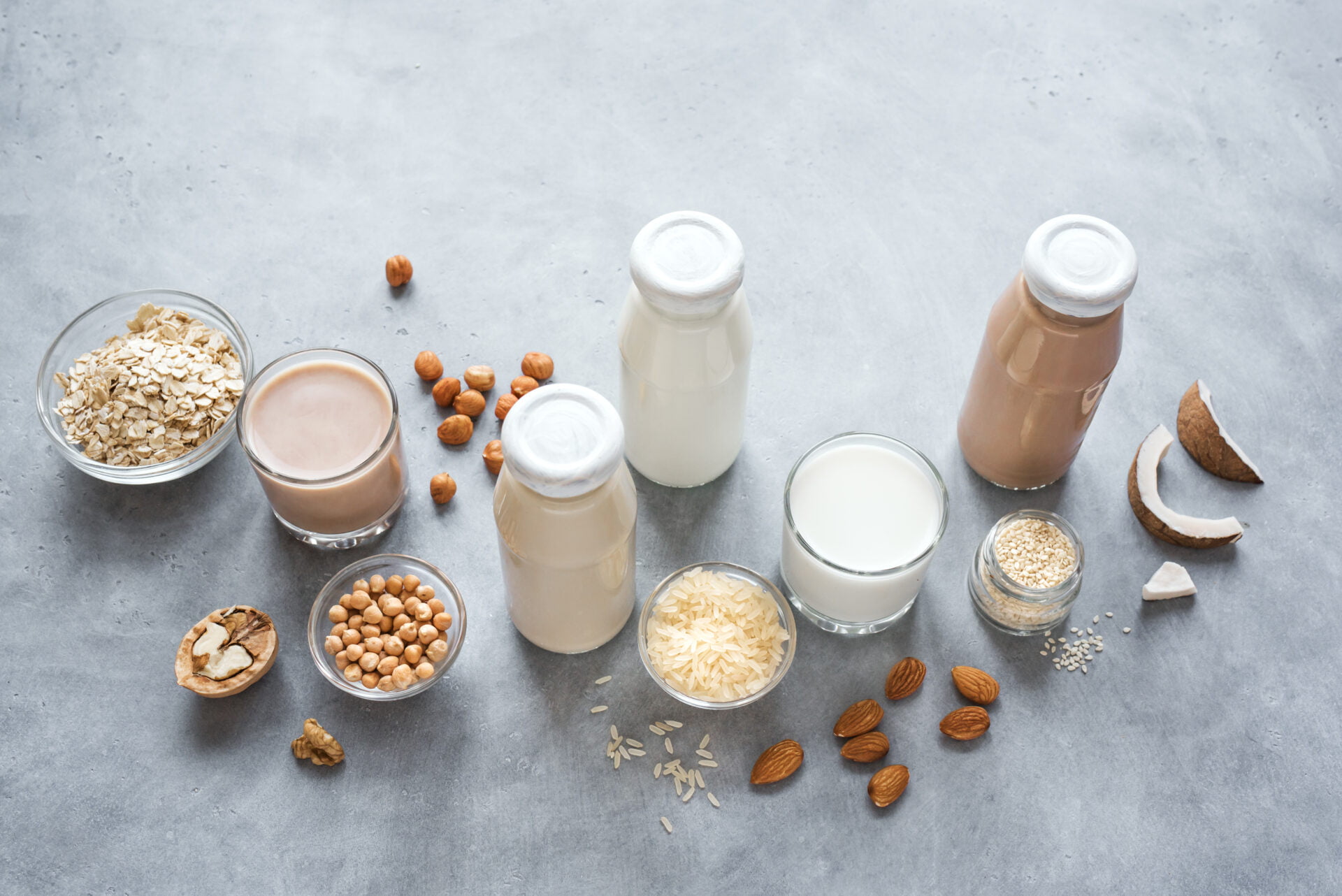 Various vegan plant based milk and ingredients on grey, copy space. Dairy free milk substitute drink, healthy eating.