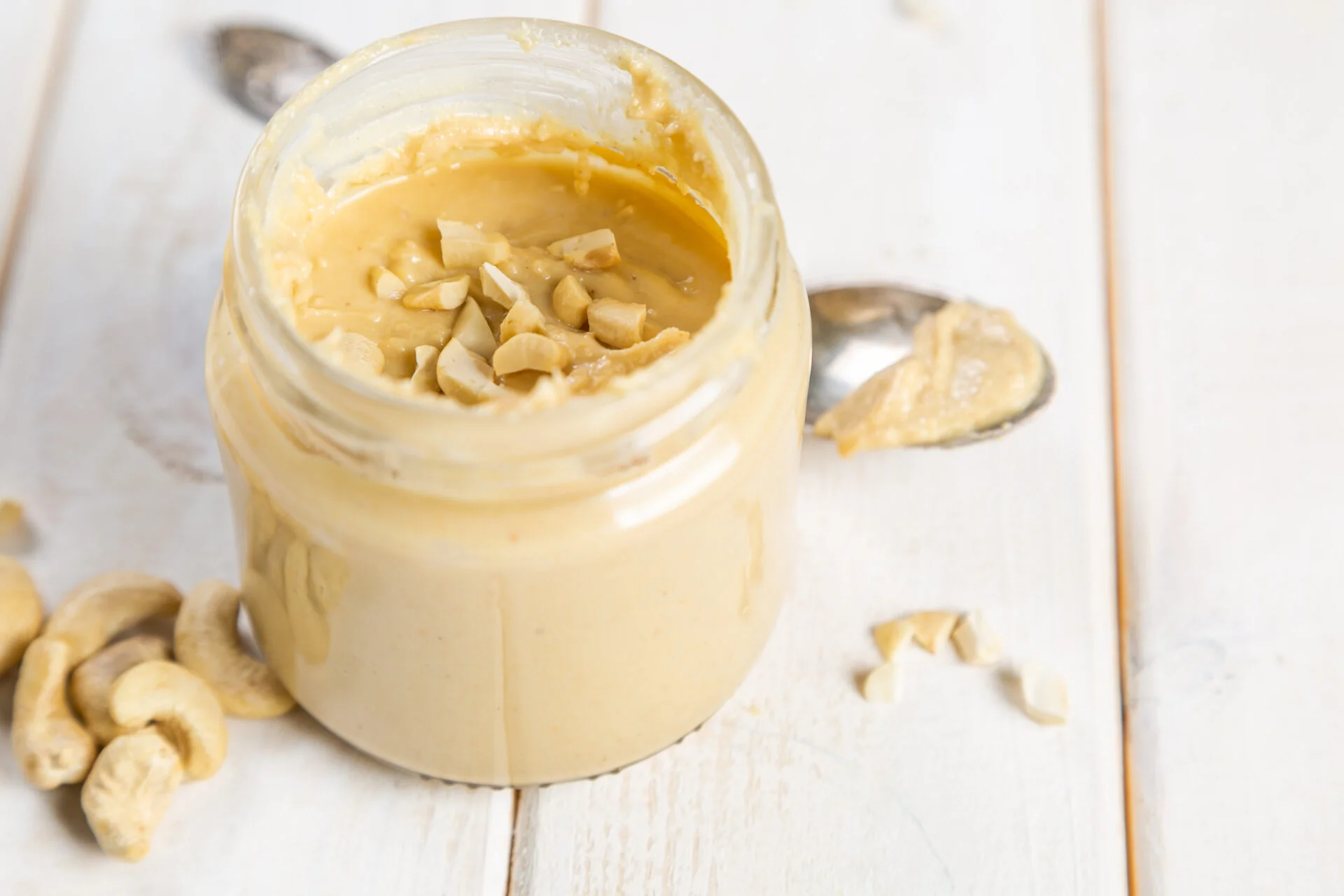 Cashew butter in glass jar, white wood background