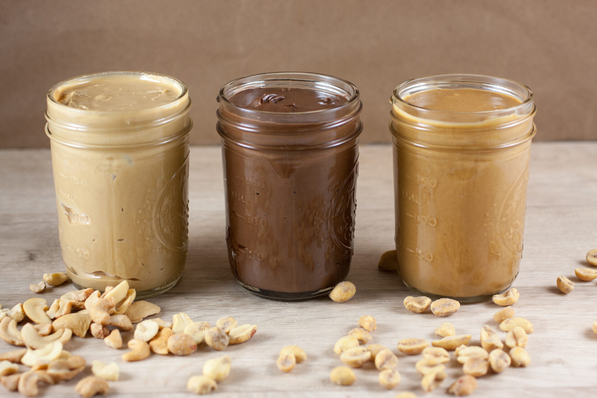 Peanut butter, hazlenut spread, and cashew butter on a wooden table