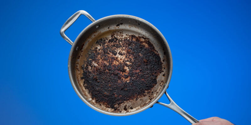 Dirty oily burnt metal frying pan held in hand