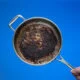 Dirty oily burnt metal frying pan held in hand