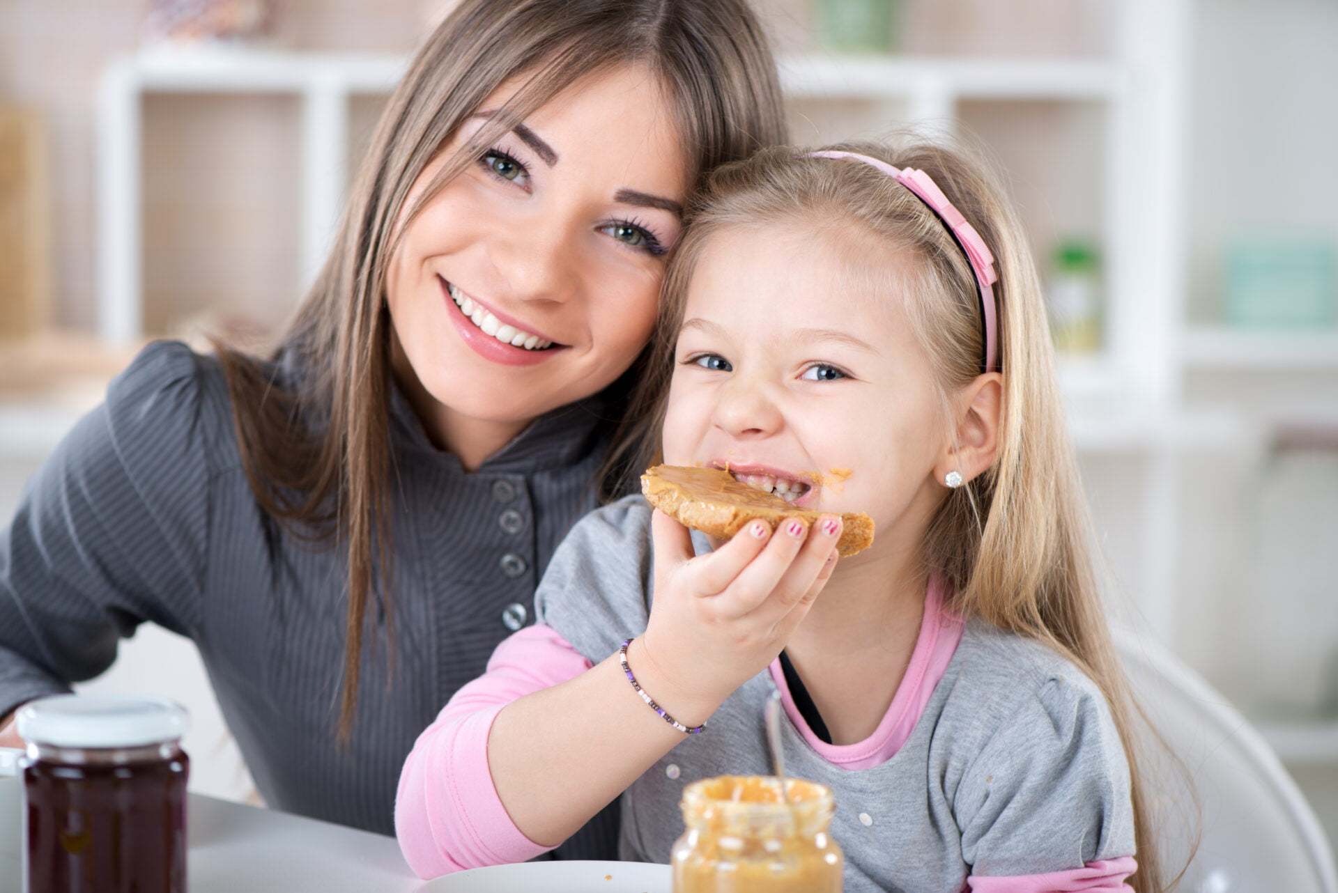 Mother and daughter breakfast in the kitchen. Cute little girl eats bread with peanut butter