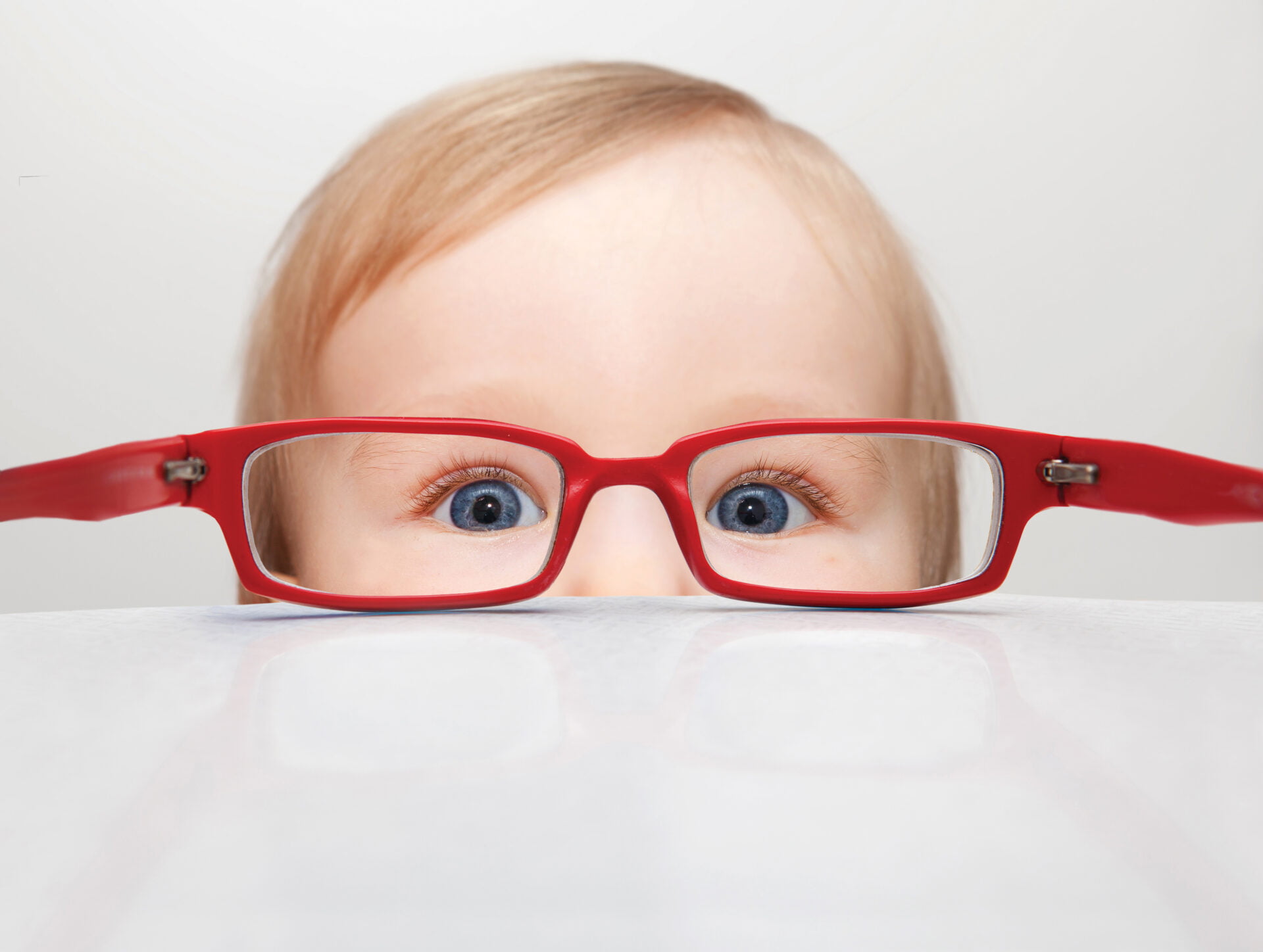 Little boy with red glasses peeking over the table