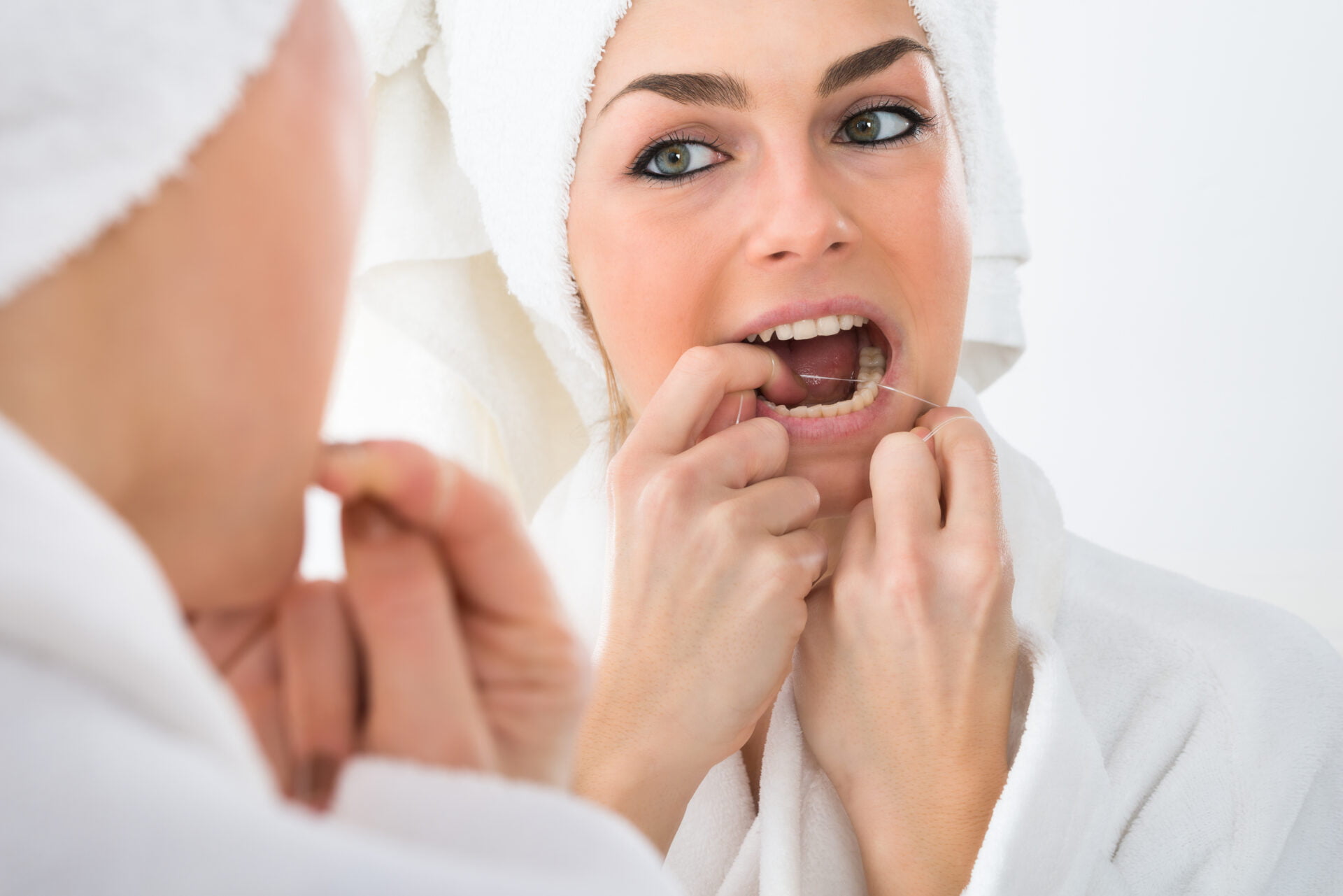 Close-up Of A Woman Looking In Mirror Flossing Teeth with bath towel on her head