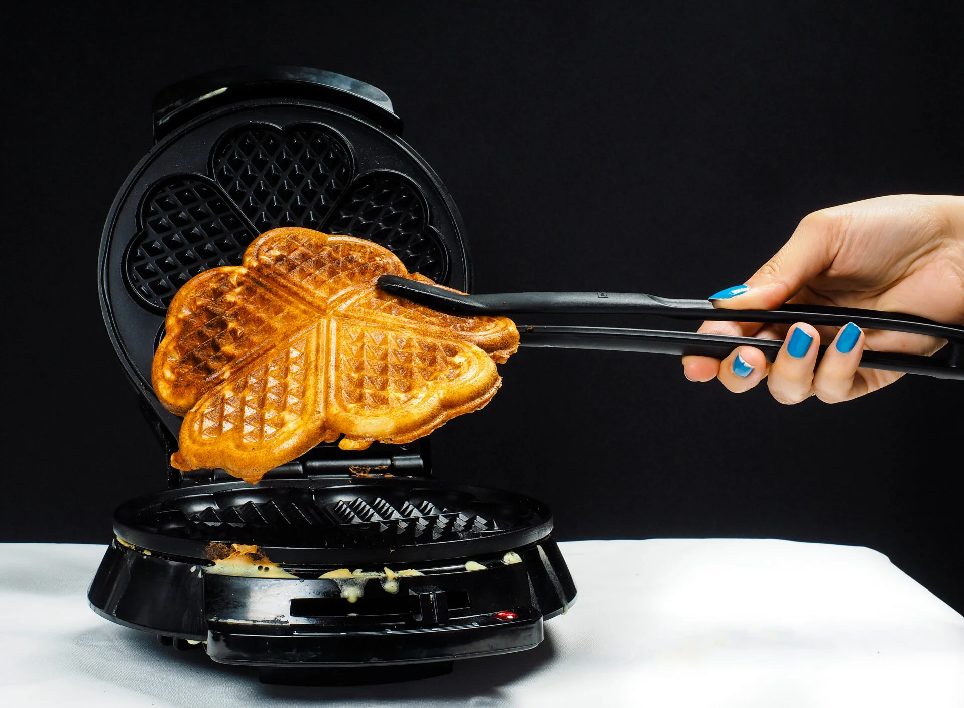 Person making fresh waffles with a waffle maker towards black on white