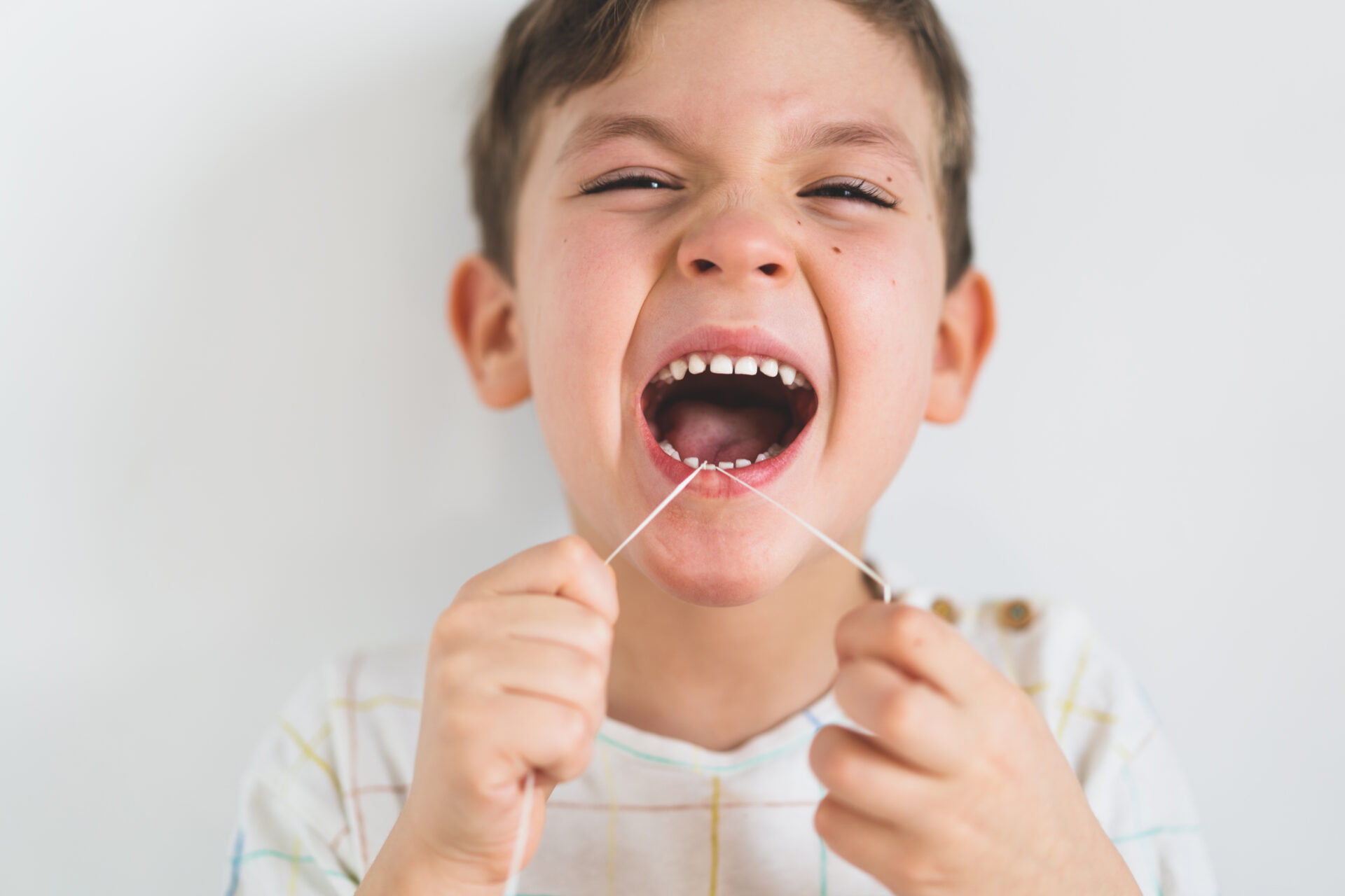 Cute boy pulling loose tooth using a dental floss. The boy's first milk tooth is loose. Toothache. Process of removing a baby tooth