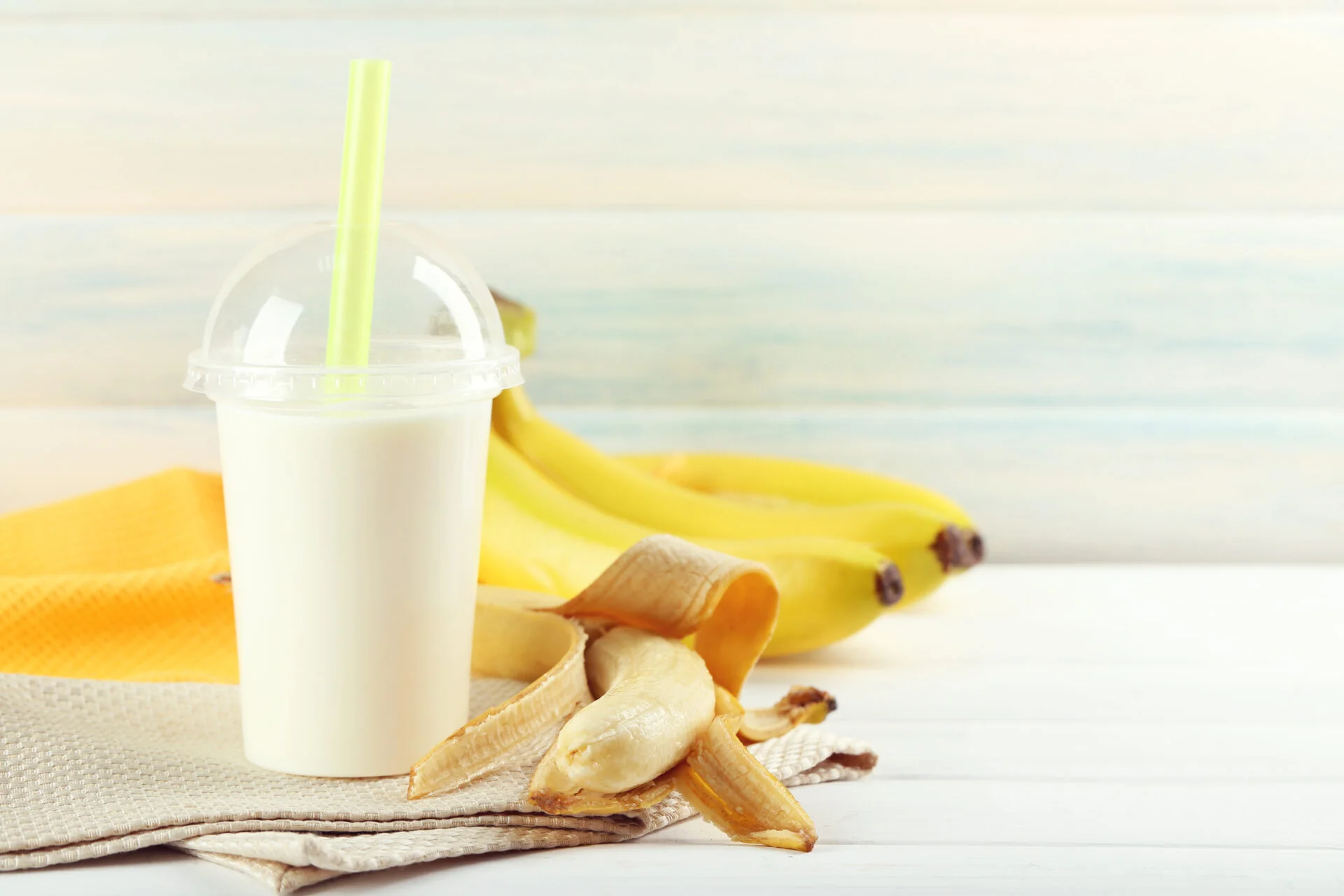 Plastic cup of milkshake with banana on color wooden background