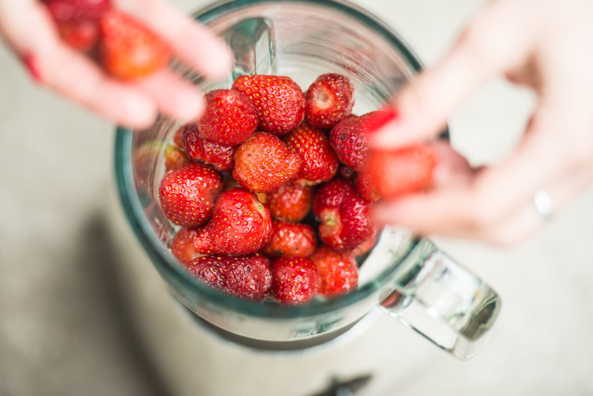 Fresh strawberries putting in blender cup and hands with some berries are blurry