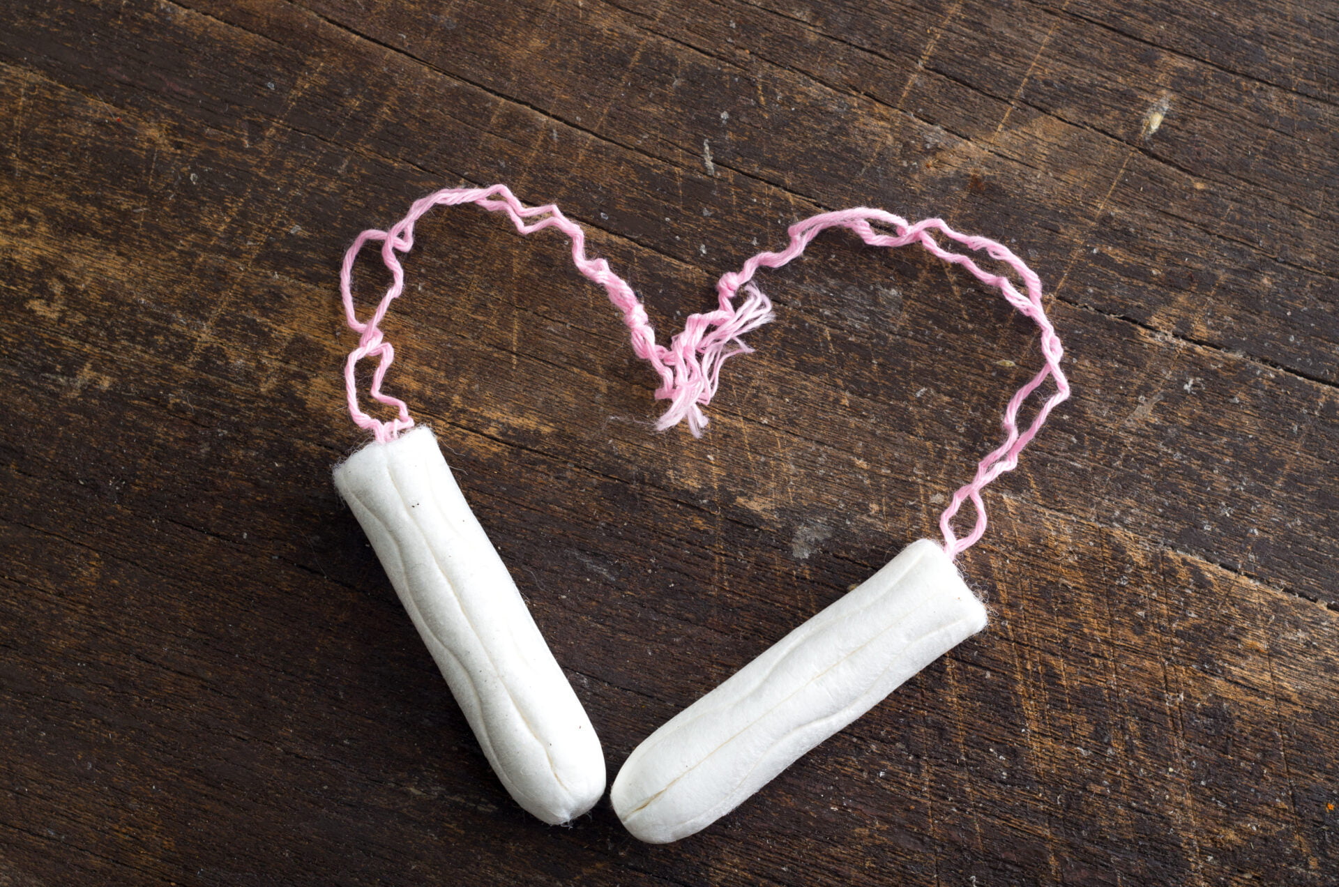 Two clean white tampons shaped in to a heart lying on wooden surface.