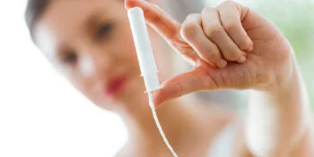 Shot of pretty young woman holding and looking tampon in the bathroom.