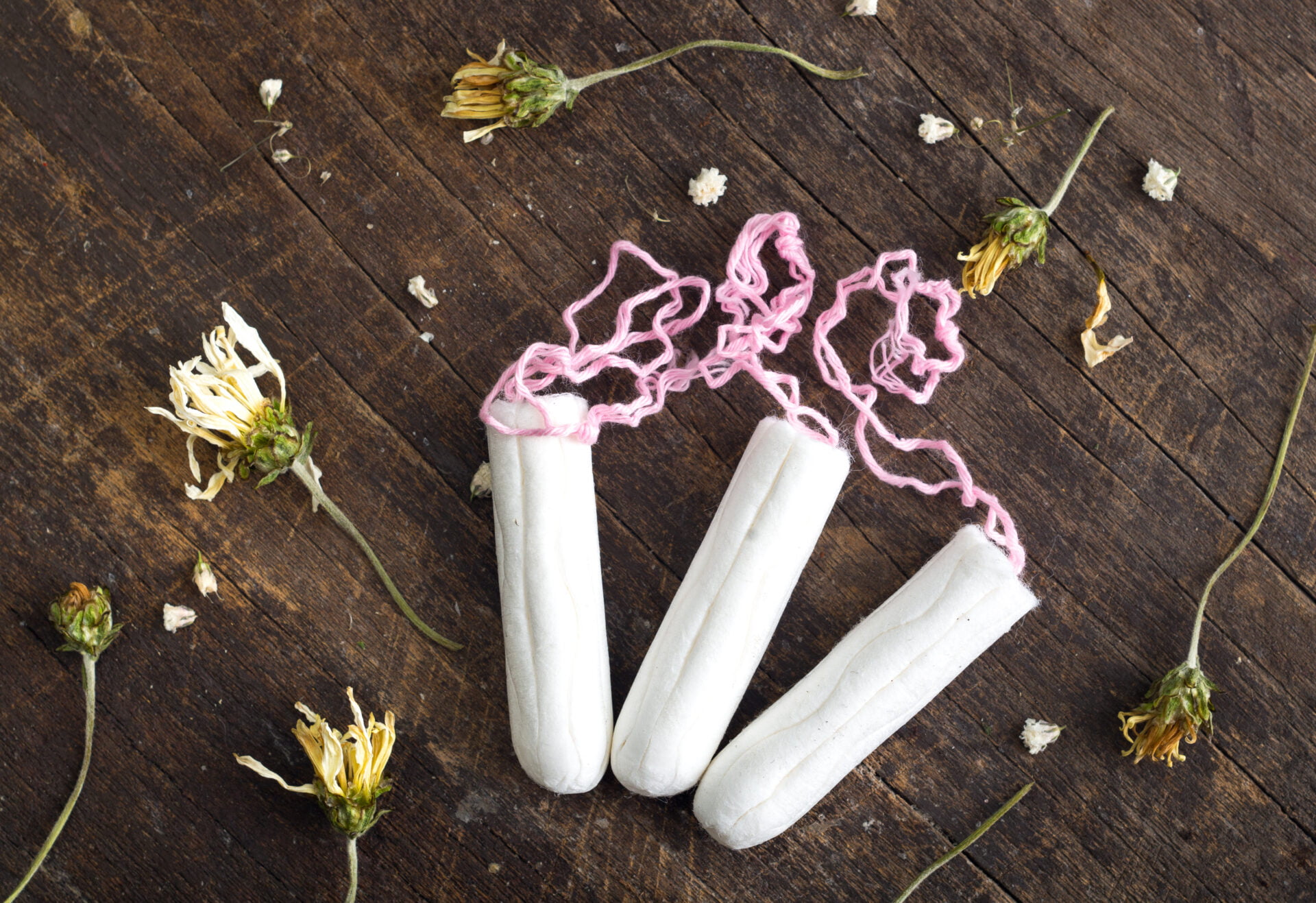 Clean white tampons lying on wooden surface with yellow colored dry flowers