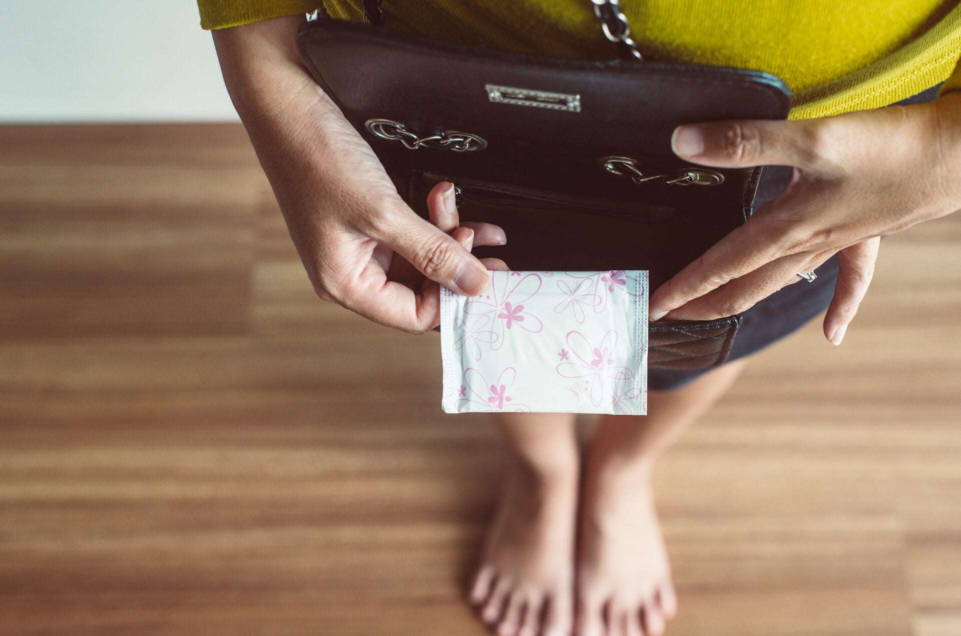 Woman hands putting sanitary napkin in handbag, White menstrual pad