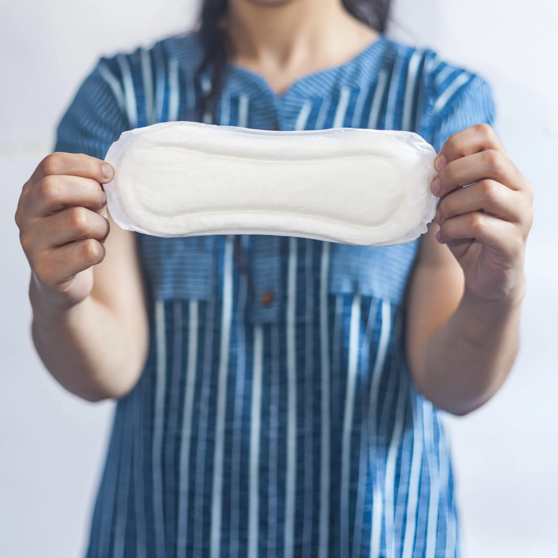 Female's hygiene products. Woman in medical gloves holding sanitary pads against the white background. Period days concept showing feminine menstrual cycle.