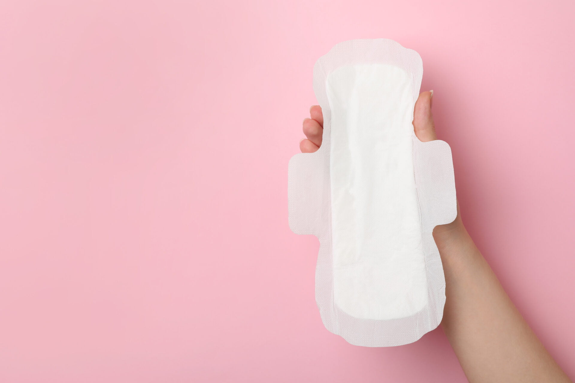 Woman holding sanitary napkin on pink background, closeup.