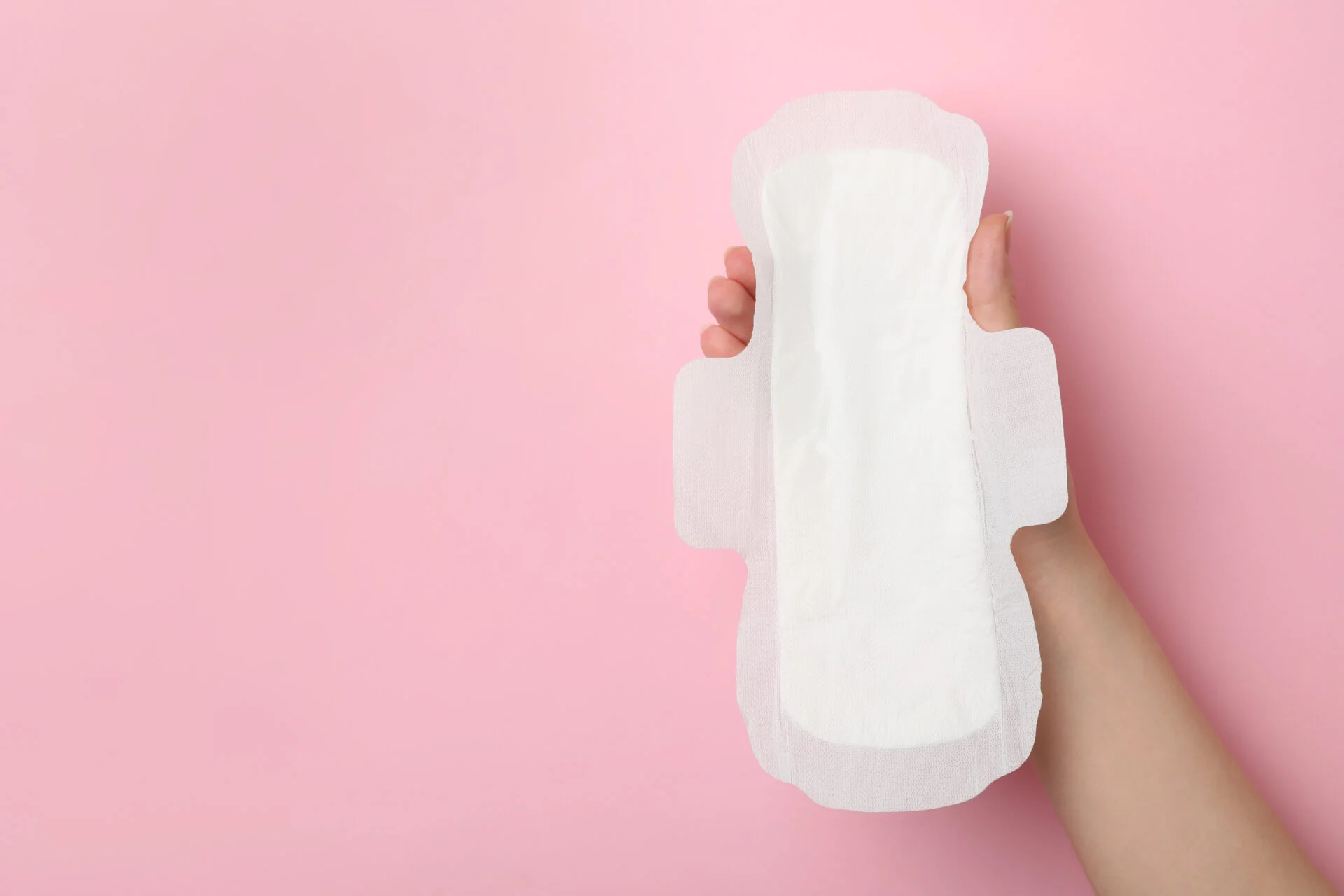 Woman holding sanitary napkin on pink background, closeup.