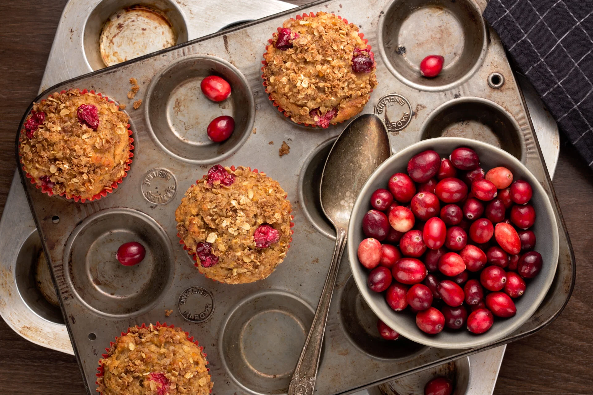 Freshly baked cranberry muffins with oatmeal crumble topping in a rustic muffin tin.