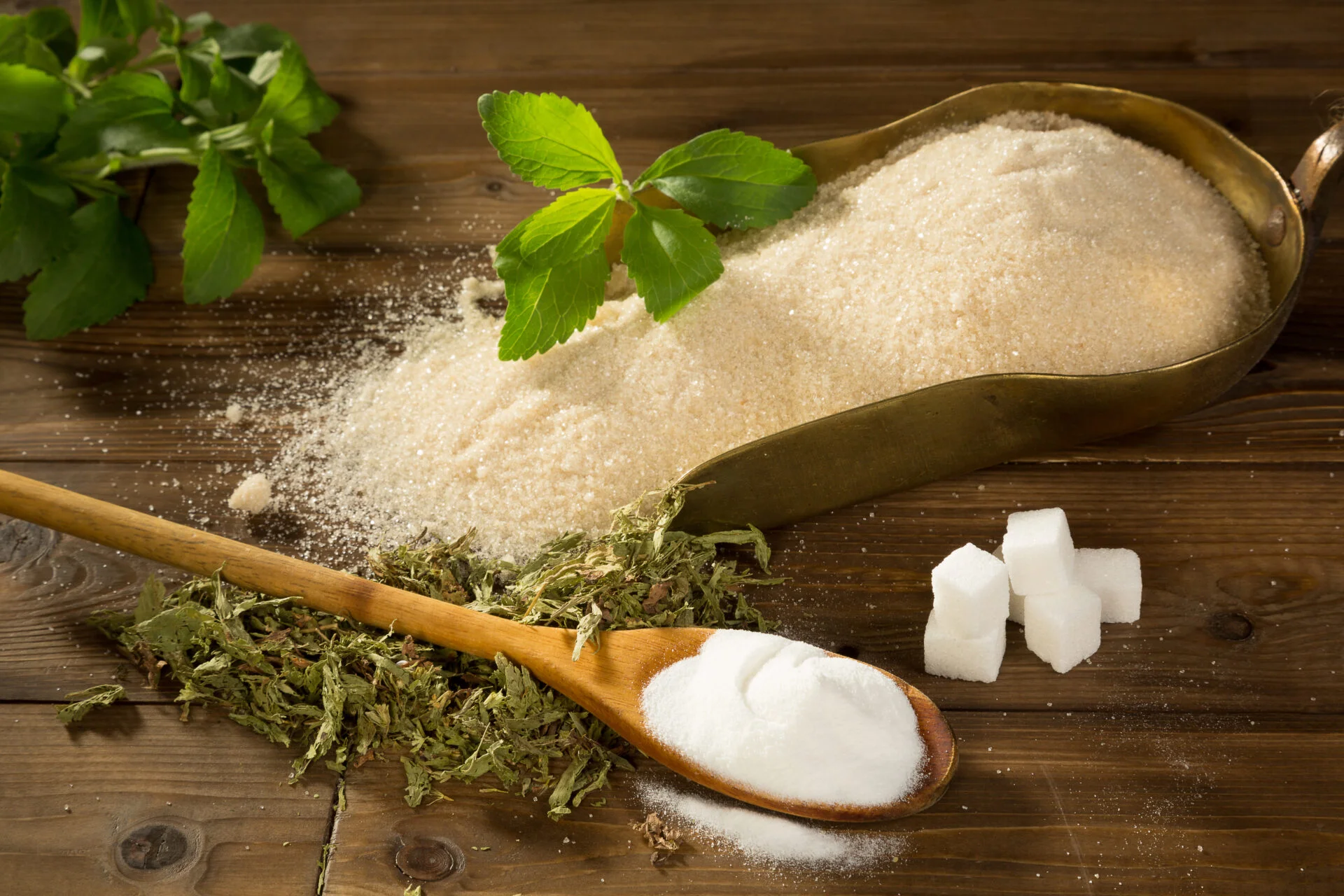 Crystal sugar and lumps together with powder and dried stevia natural sweetener on a wooden table