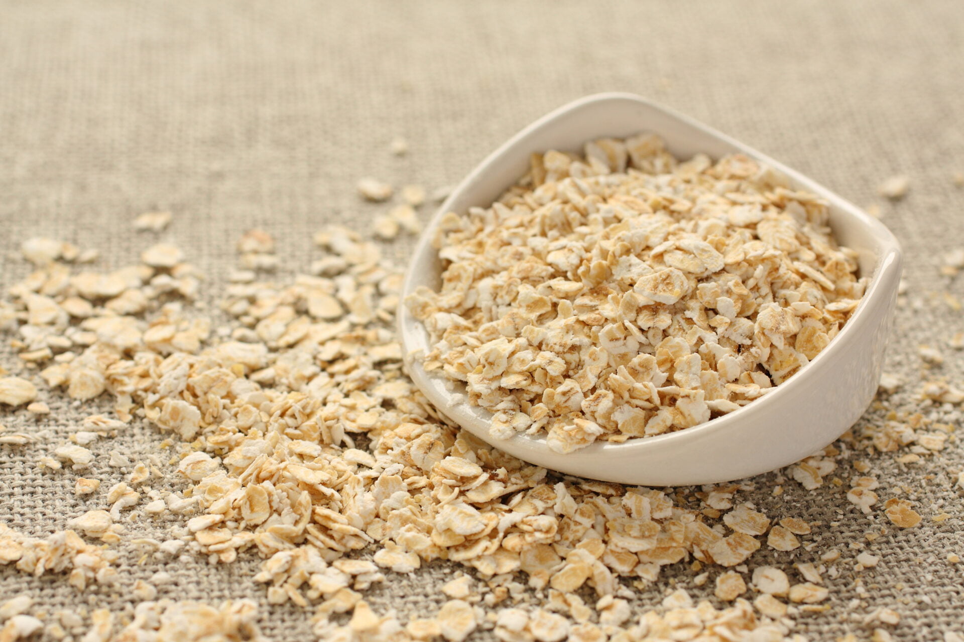Oat flakes in white ceramic bowl on sackcloth background