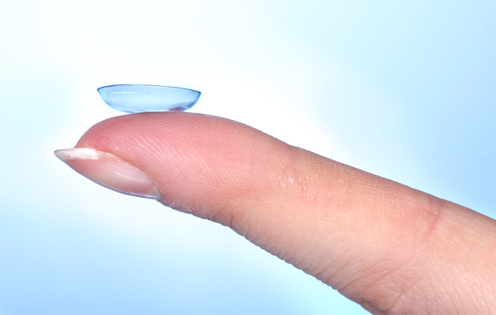 contact lens on finger on blue background