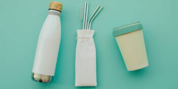 Reusable eco friendly sustainable bamboo cup, stainless steel metal straws and water bottle on light blue background. Flat lay.