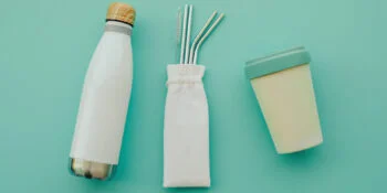 Reusable eco friendly sustainable bamboo cup, stainless steel metal straws and water bottle on light blue background. Flat lay.