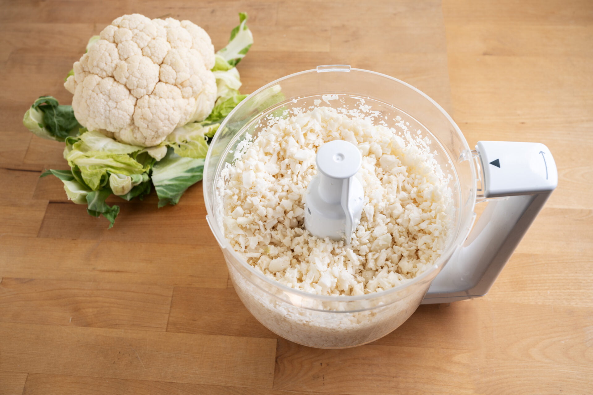 cauliflower shredded in a food processor for healthy low carb pizza crust or as vegetable rice replacement on a wooden kitchen table