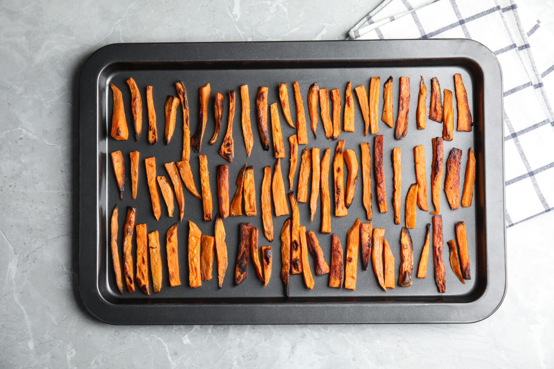 Baking sheet with sweet potato slices on grey background, top view