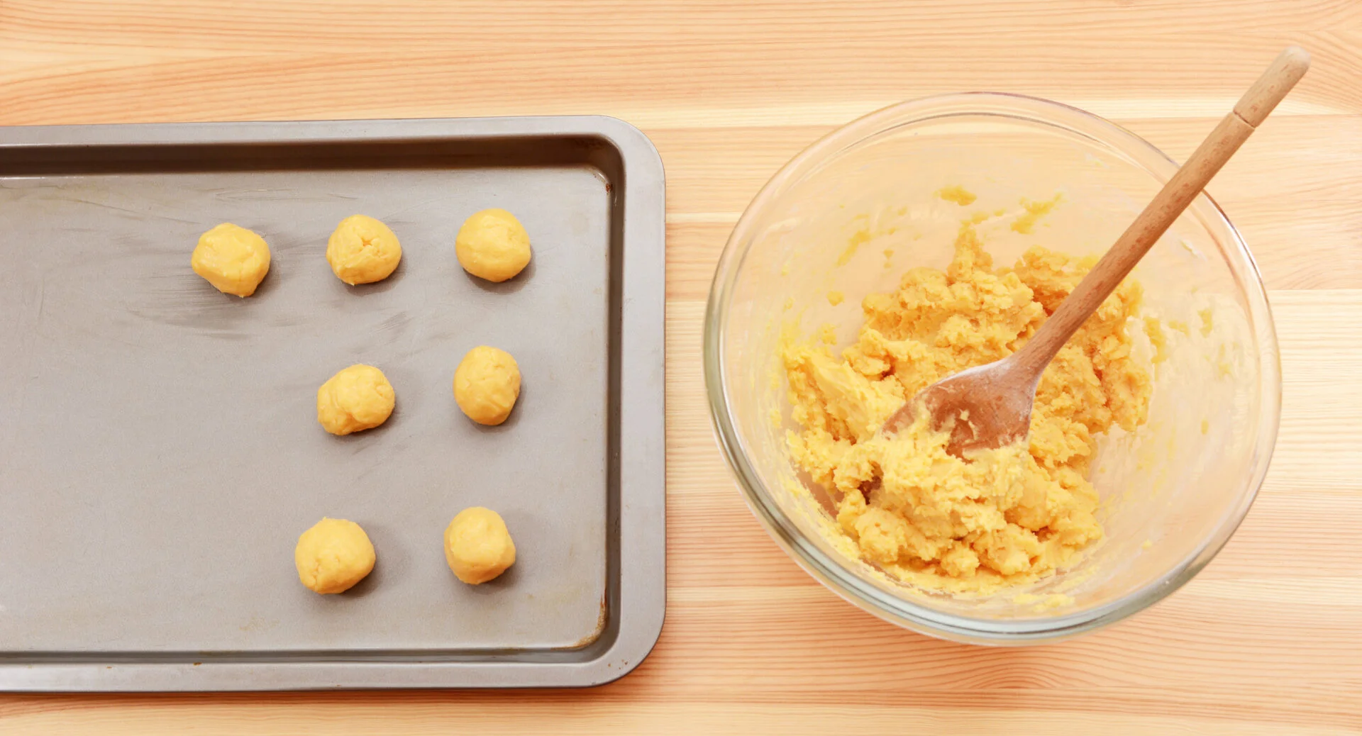 Adding balls of cookie dough to a baking sheet from a bowl of raw mixture