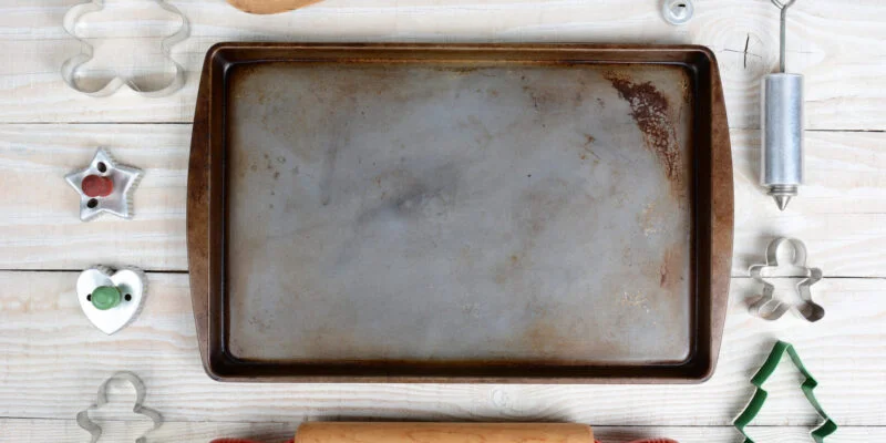 Overhead shot of a group of items for baking Christmas Cookies surrounding an empty cookie sheet. Horizontal format on a rustic wood kitchen table.