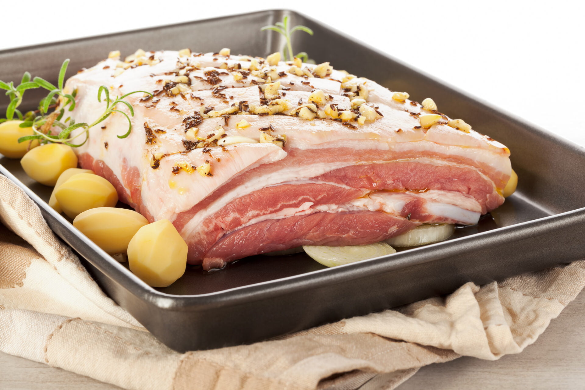 Delicious raw pork belly with fresh herbs and potatoes on baking tray. Luxurious meat eating.