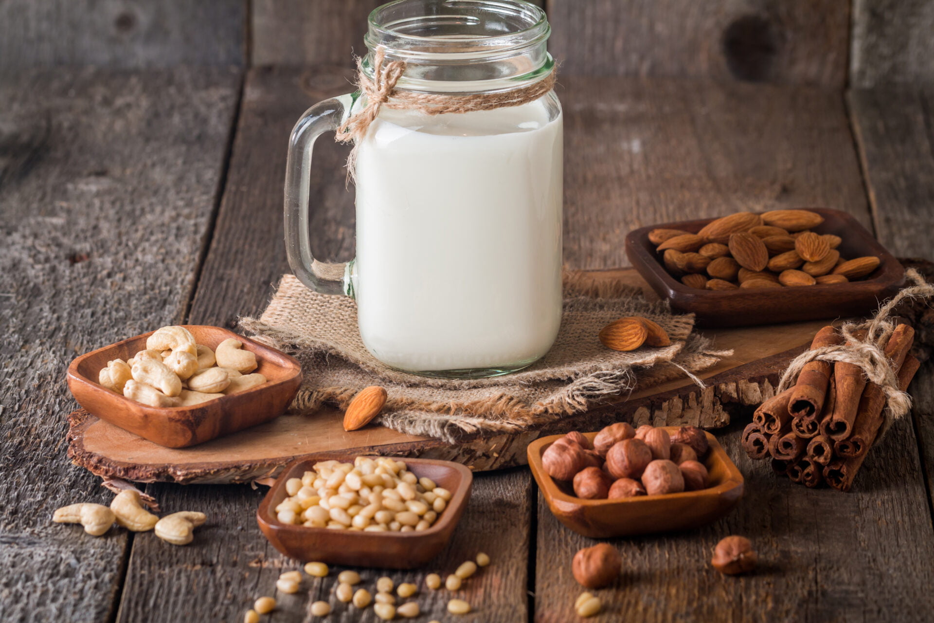 Vegan milk from nuts in glass jar with various nuts on wooden background
