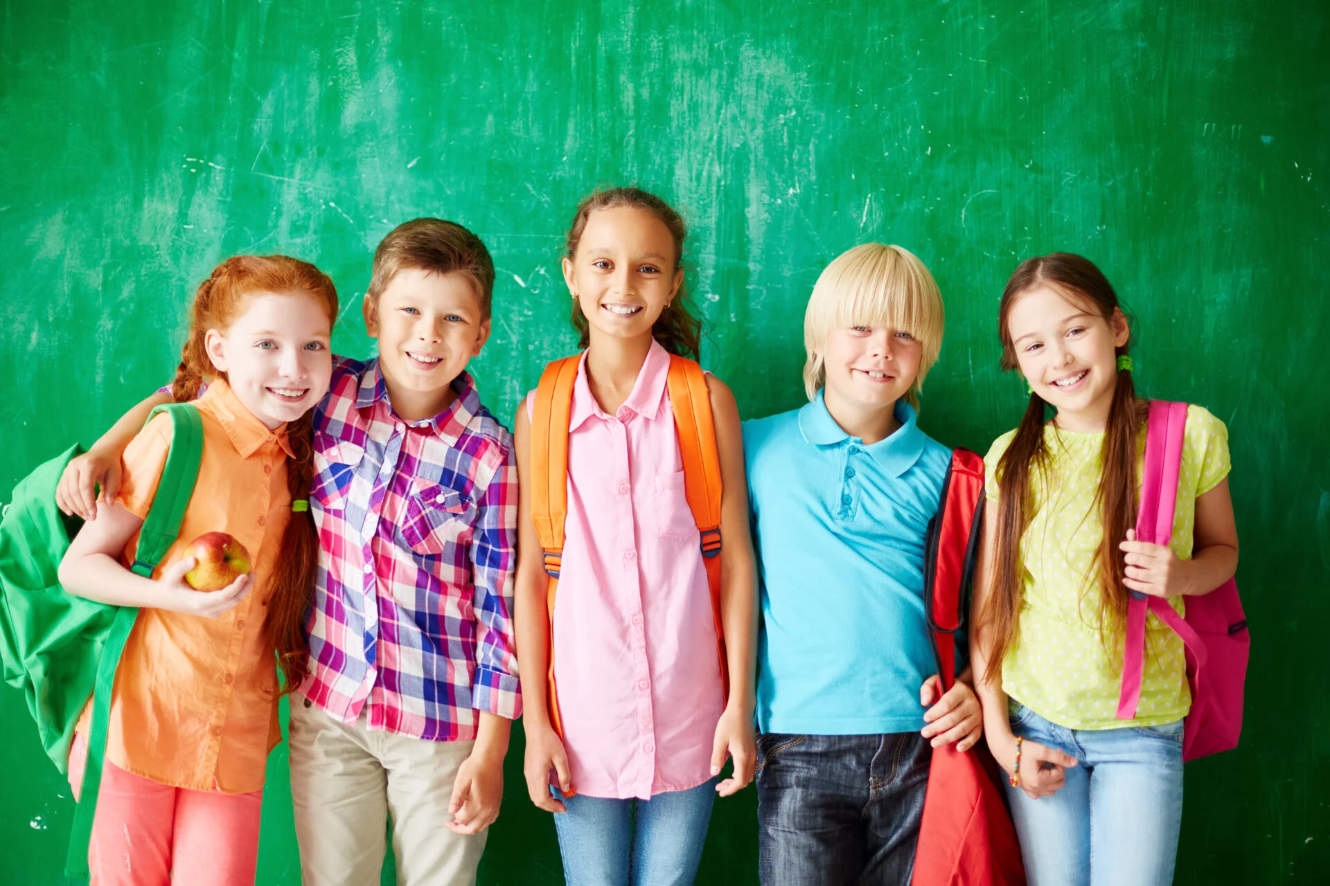 Happy kids with backpacks standing in row along school blackboard