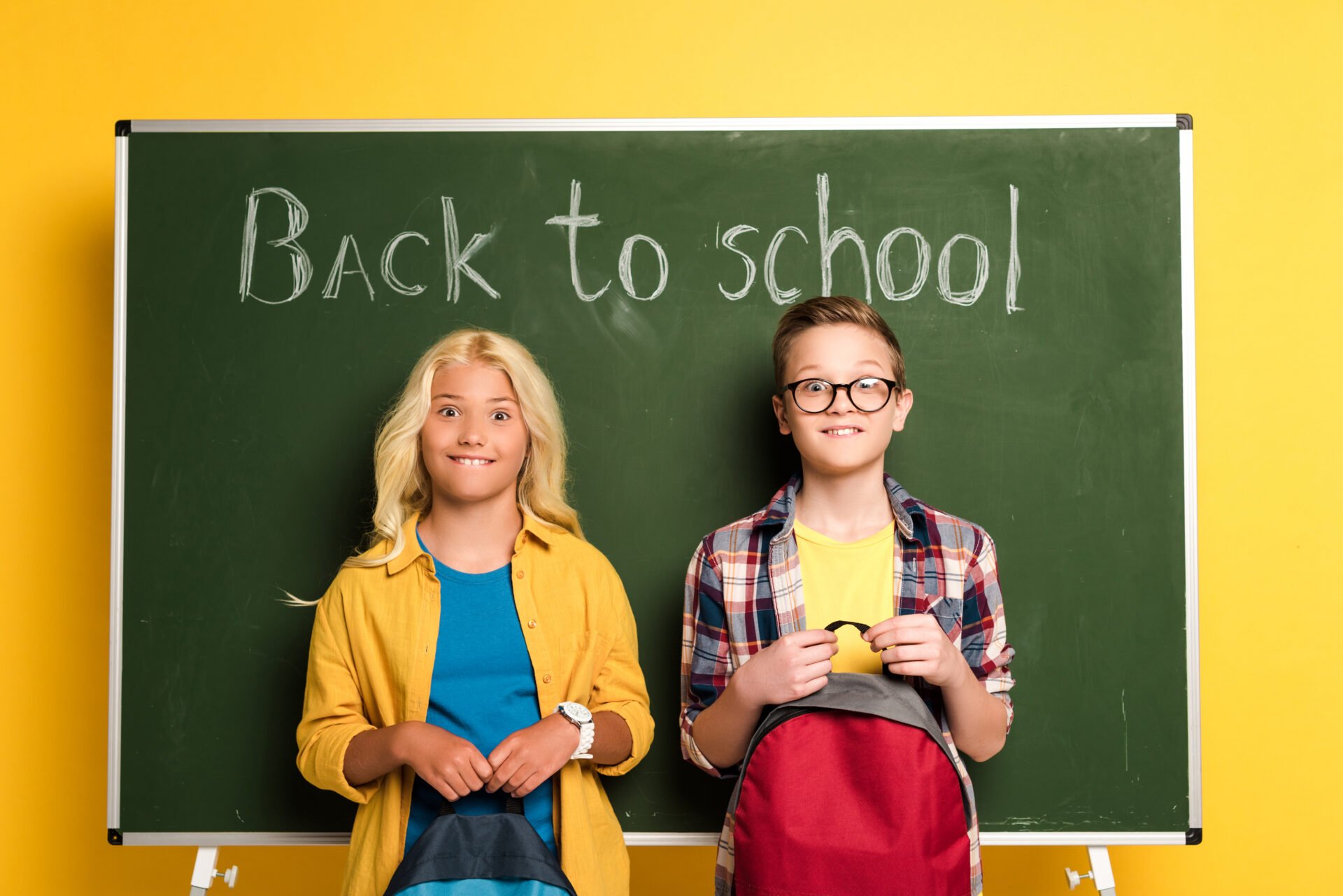 Back to school with children and their backpacks standing in front of a chalkboard
