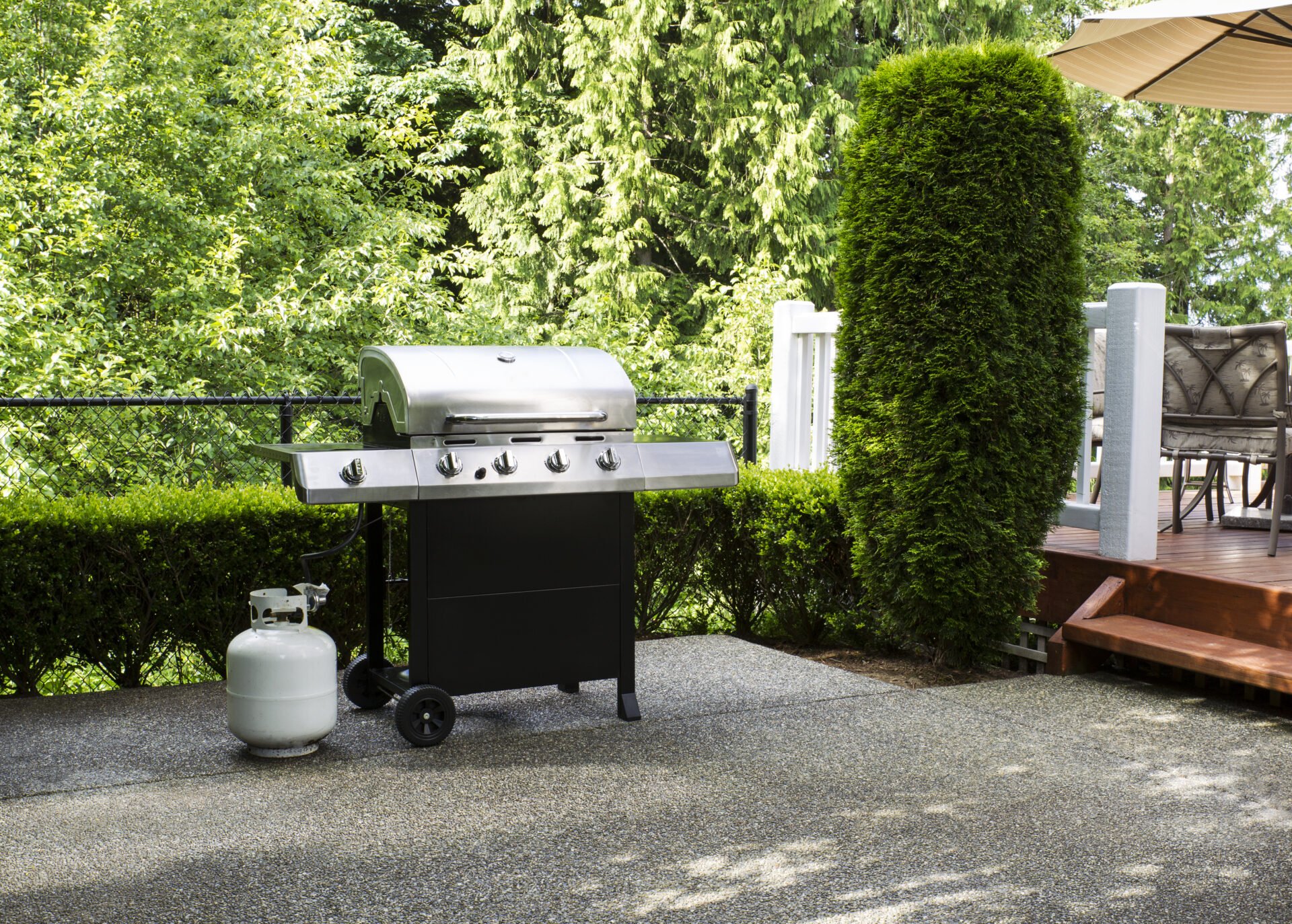 Horizontal photo of a large barbeque cooker on concrete outdoor patio with woods and deck in background