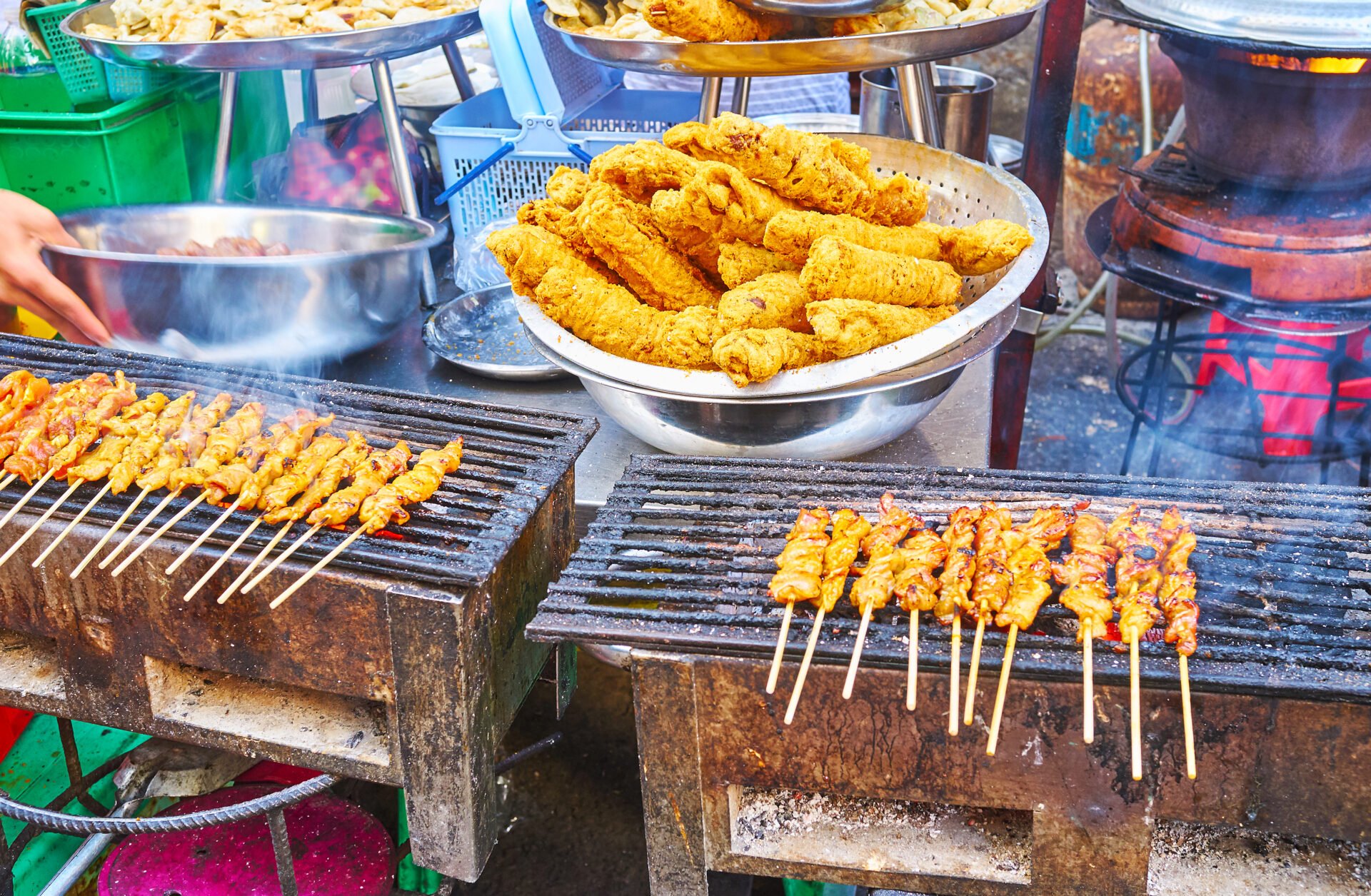Chicken on skewers and deep fried meat on grills of outdoor cafe's open air kitchen in Chinatown market, Yangon, Myanmar.